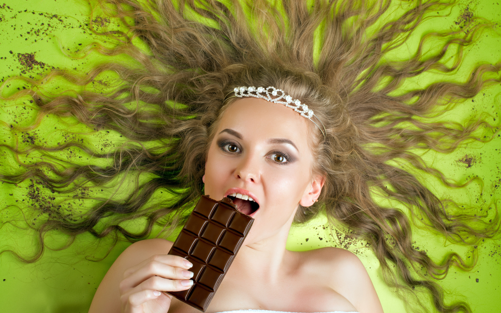 Красивая девушка с украшением в волосах лежит с шоколадкой 