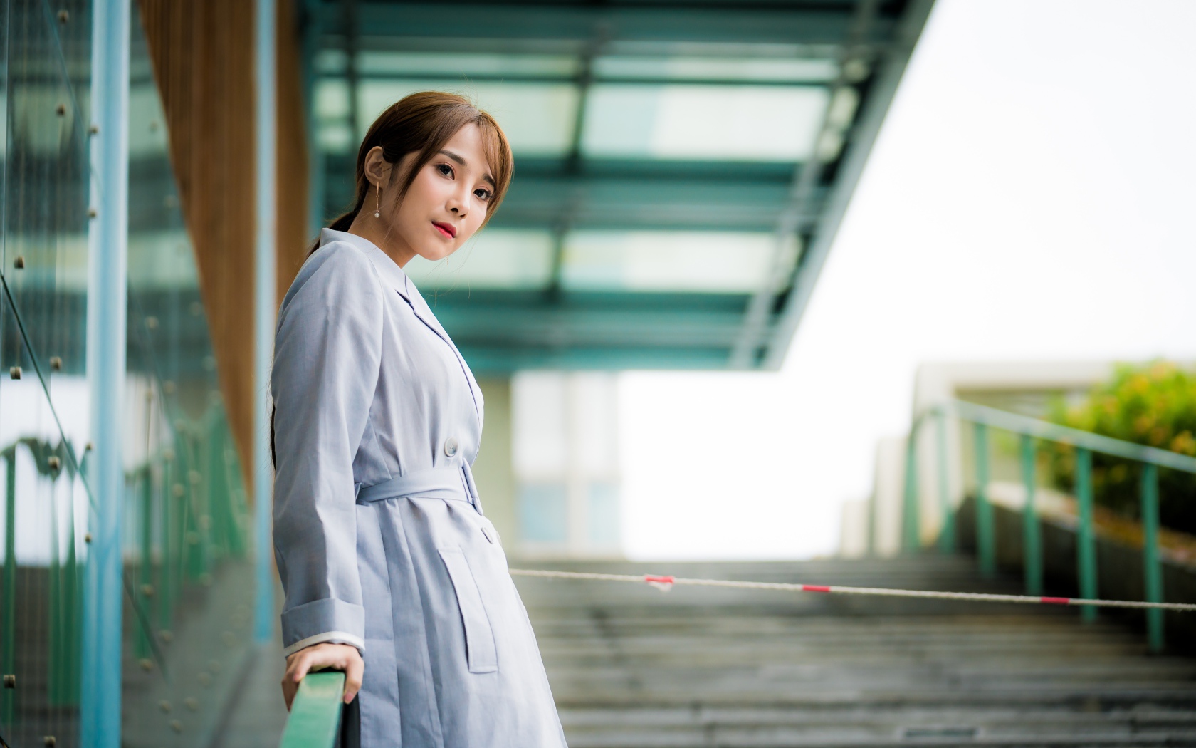 Девушка азиатка в пальто стоит у перил 