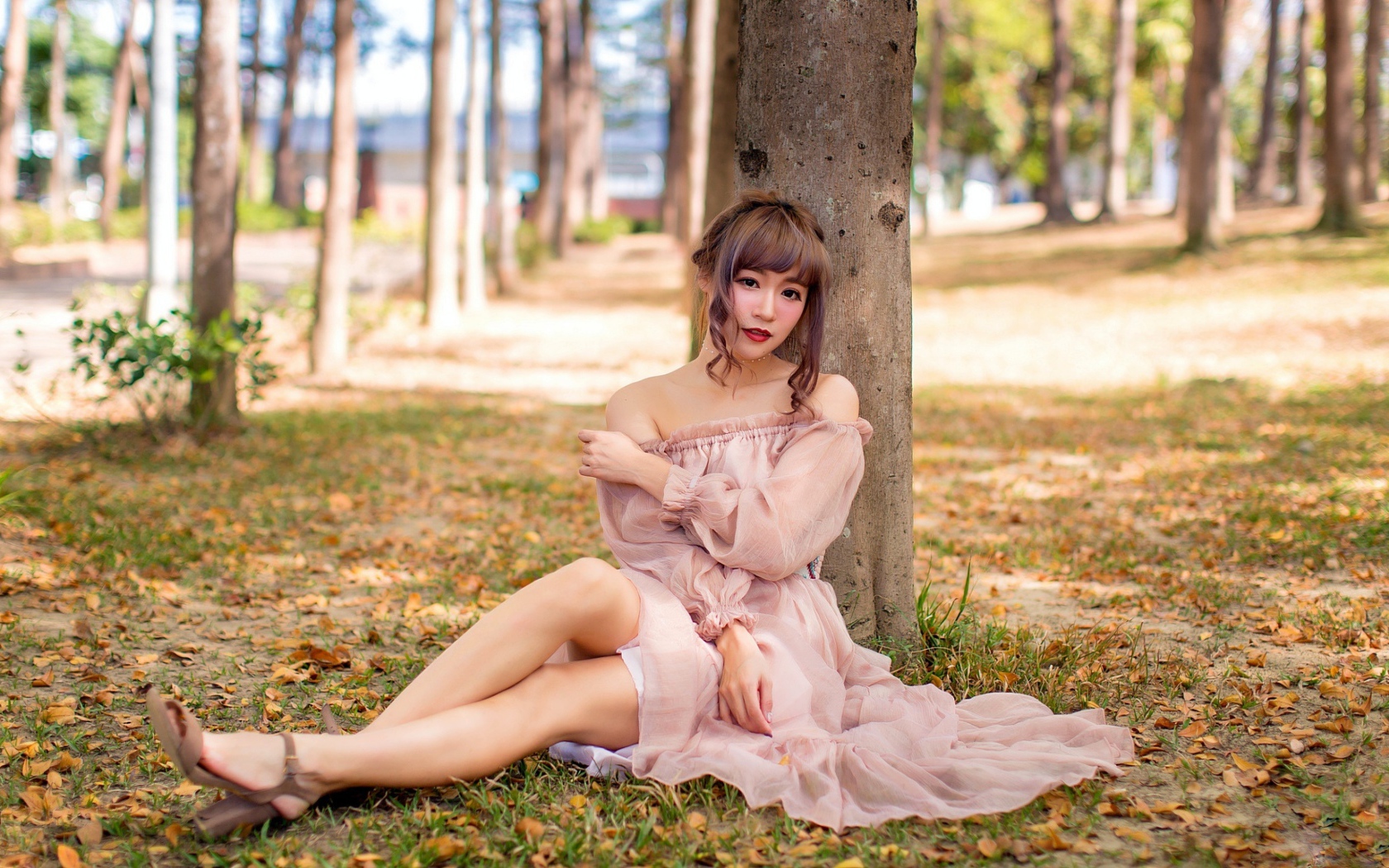 Красивая девушка азиатка в платье сидит под деревом