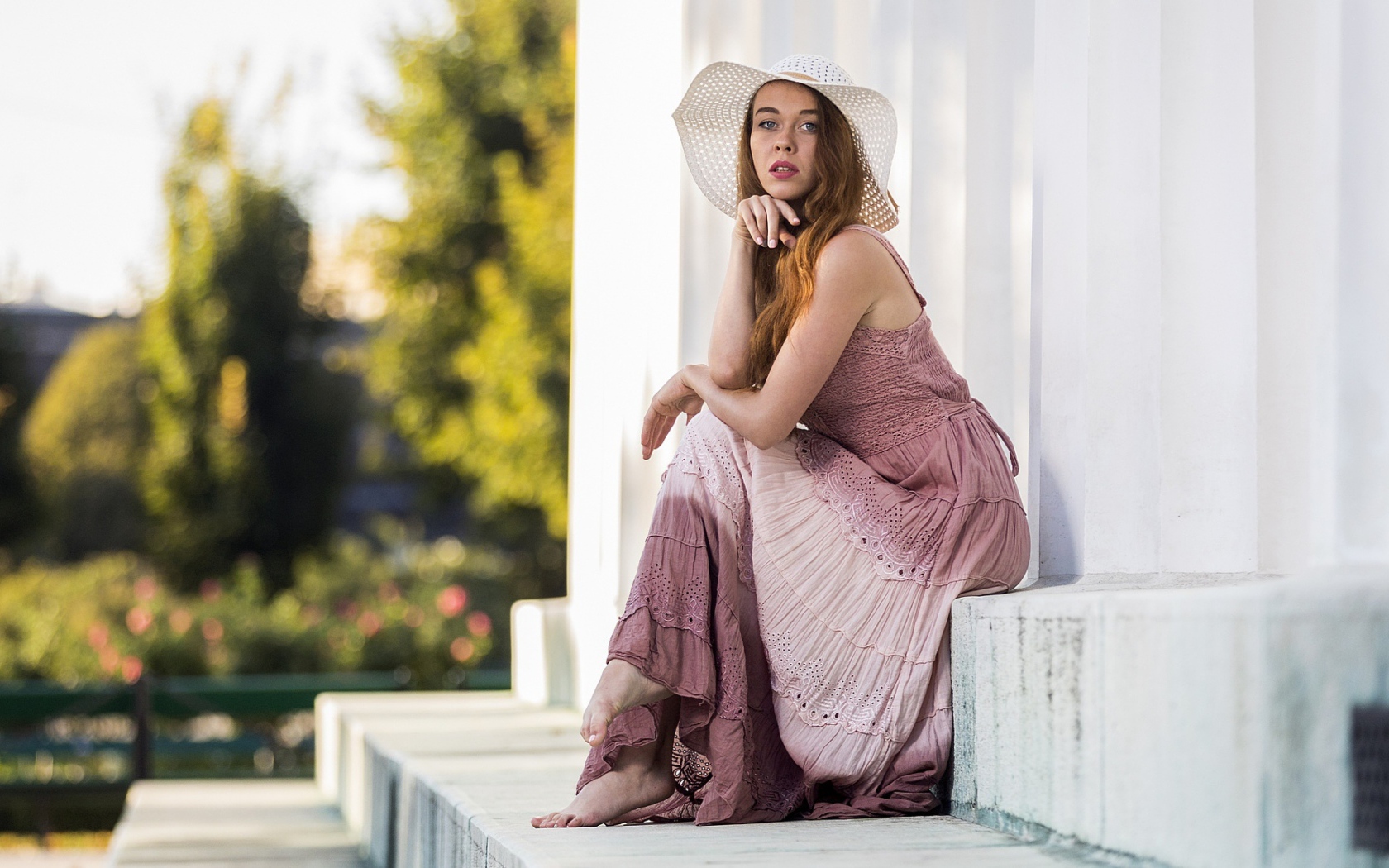 Красивая девушка в белой шляпе сидит на ступеньках 