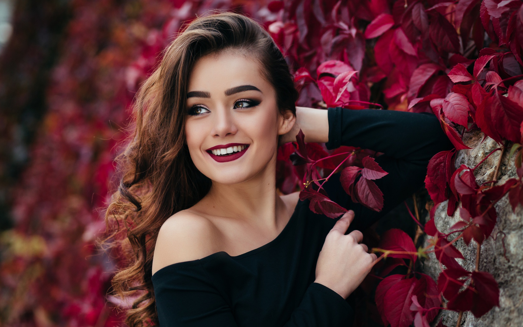 Красивая улыбающаяся длинноволосая девушка у стены с декоративным виноградом