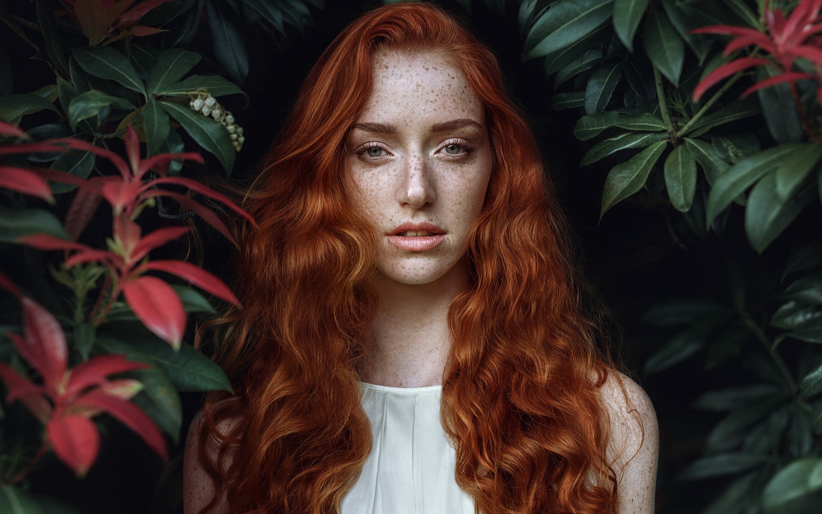 Рыжеволосая девушка с веснушками на лице на фоне кустов 