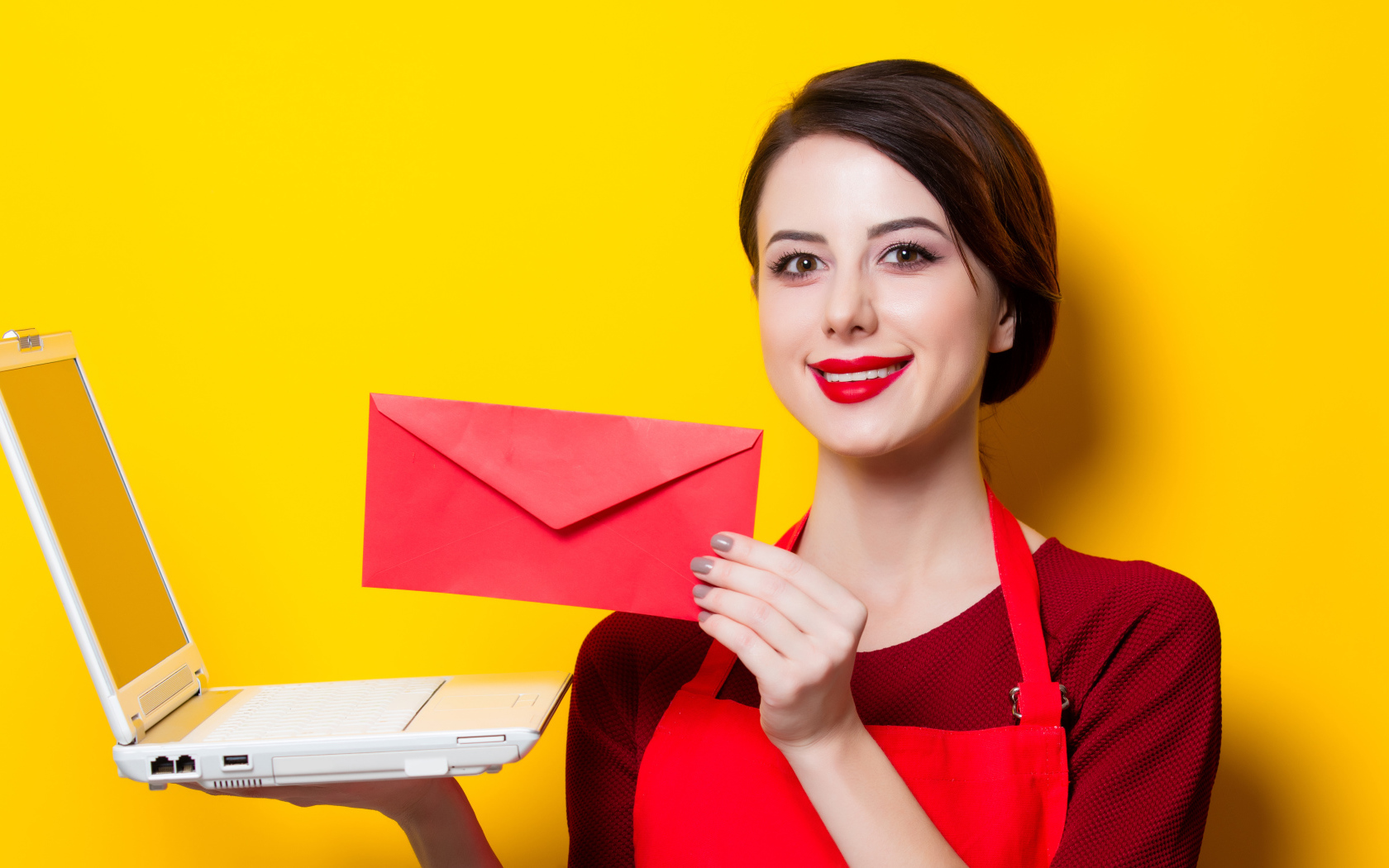 Улыбающаяся девушка с ноутбуком и конвертом в руках на желтом фоне