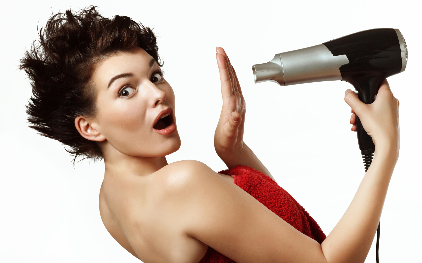 Удивленная девушка с феном в руках на белом фоне