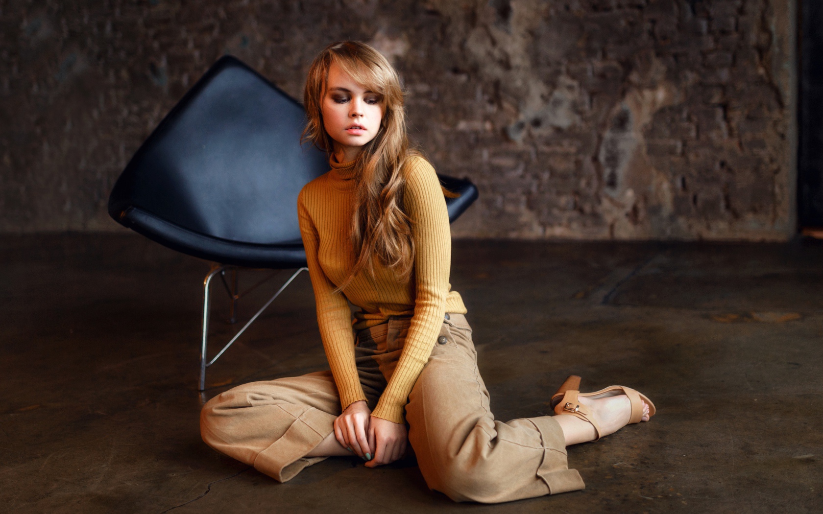 Девушка сидит на полу около черного кресла 