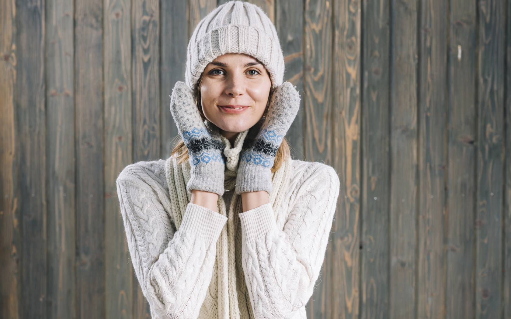 Молодая девушка на шапке, варежках  и теплой шапке на фоне забора