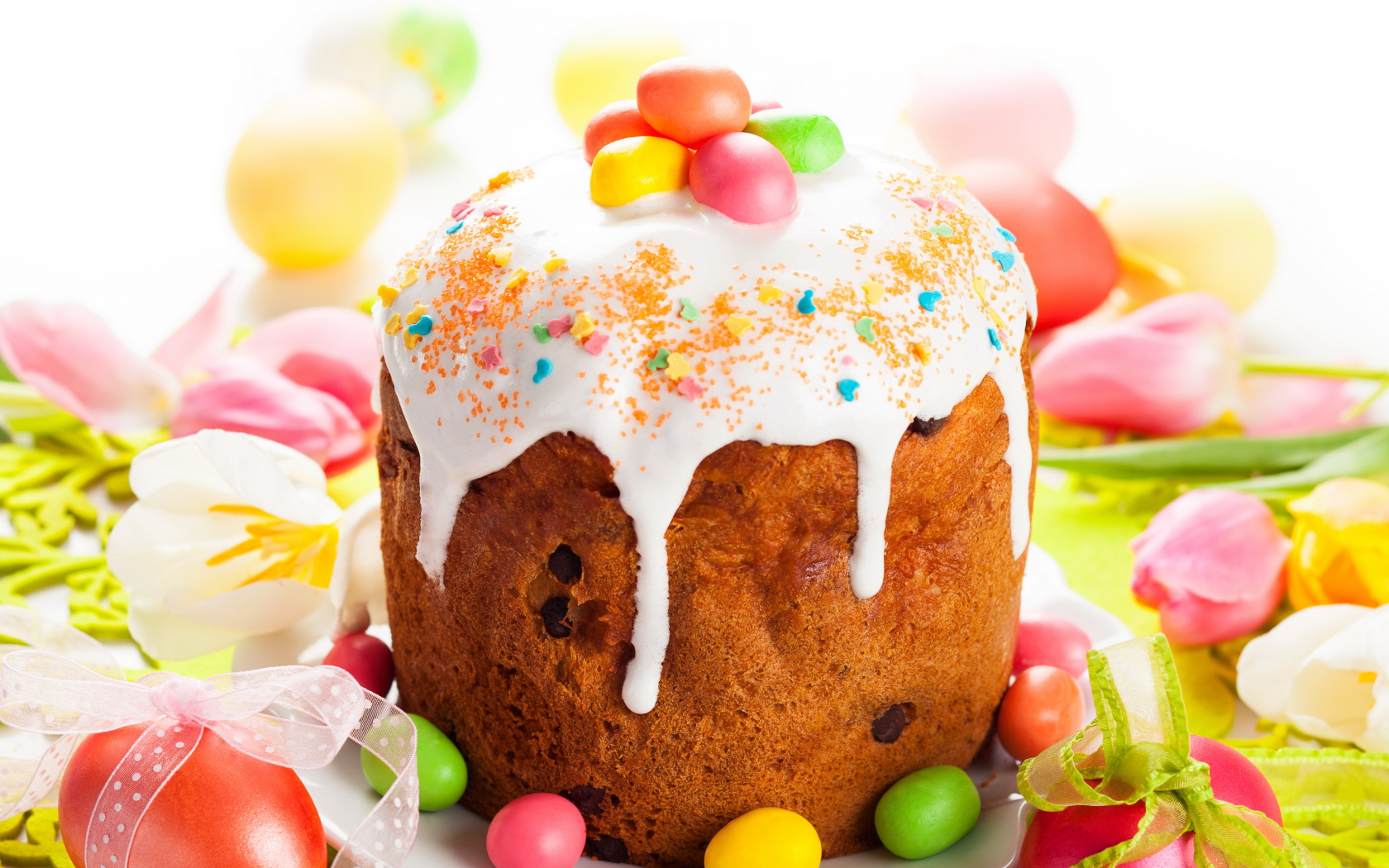 Красивый пасхальный кулич с белой глазурью и конфетами на столе с яйцами