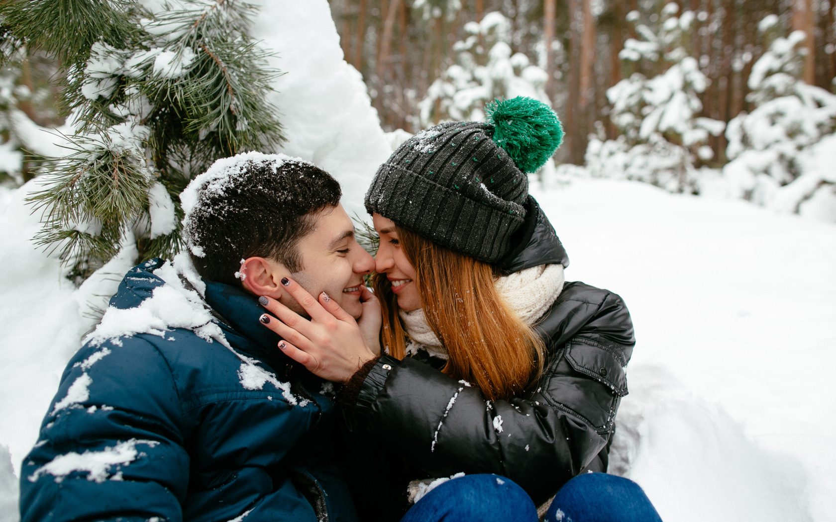 Влюбленная пара сидит под заснеженной еловой веткой зимой