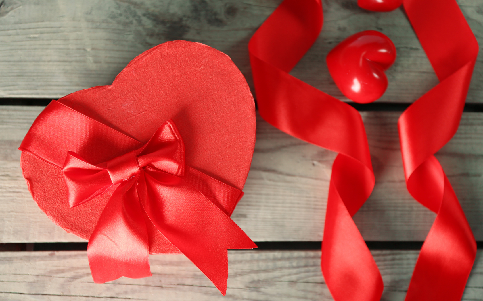 Красная коробка в форме сердца на деревянном столе с красными лентами