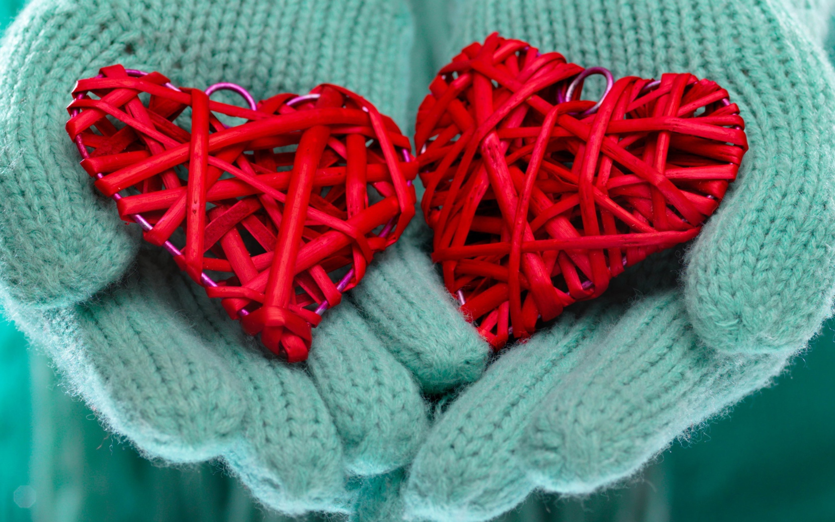 Два плетеных красных сердца лежать на руках в варежках