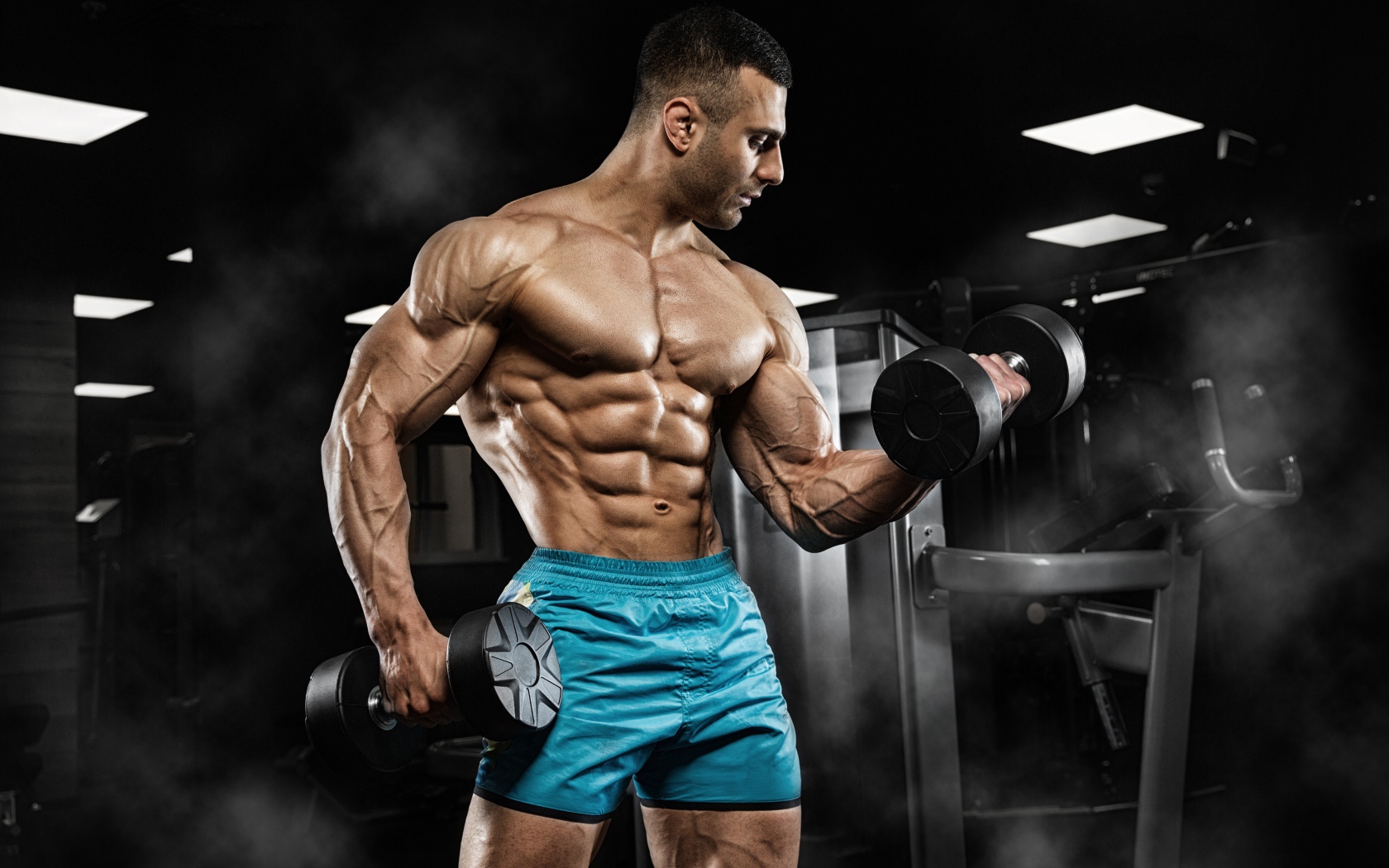Сильный накаченный мужчина в шортах с гантелями в руках 