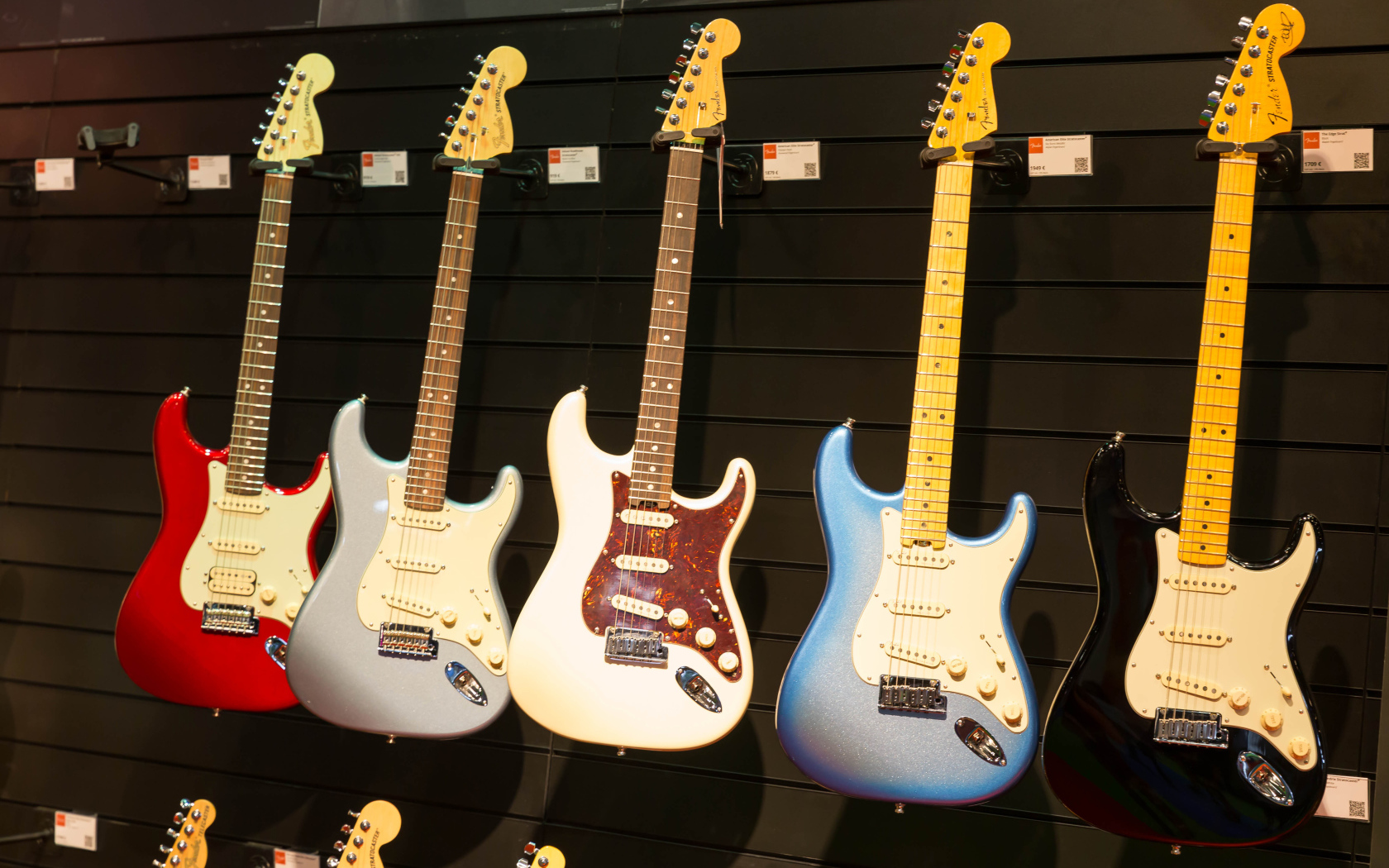 Много разноцветных электрогитар на стене 