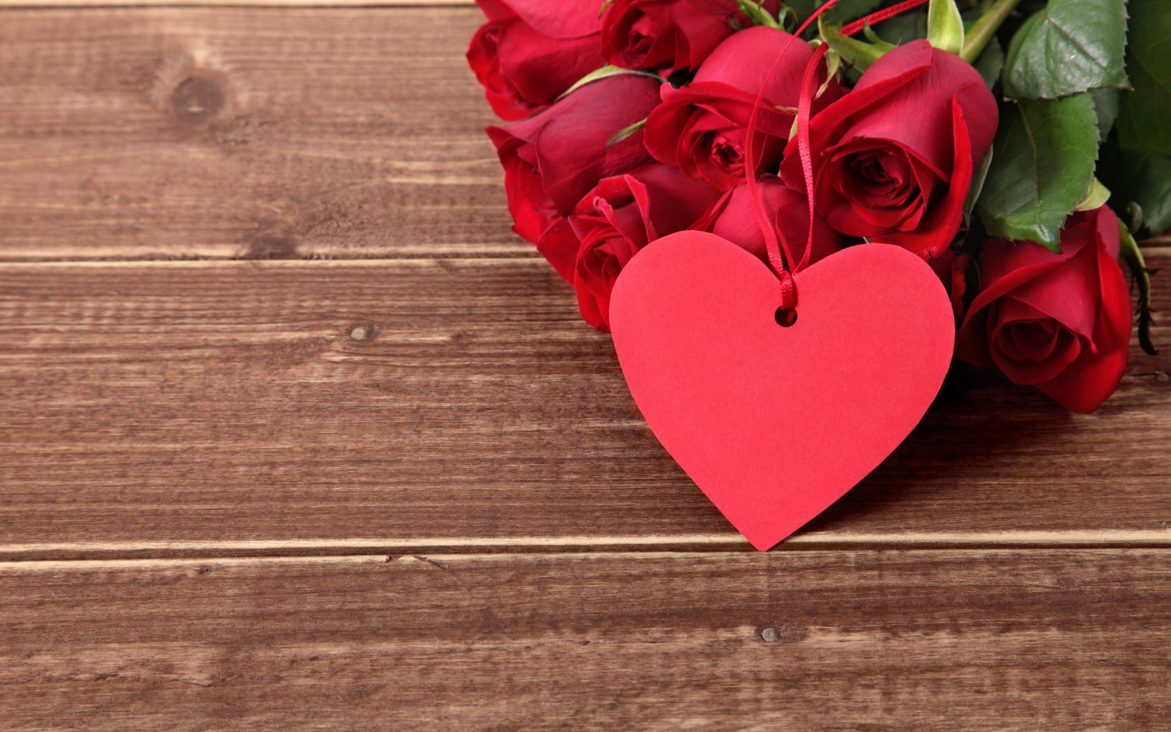 Букет красных роз на деревянном столе с красным сердцем