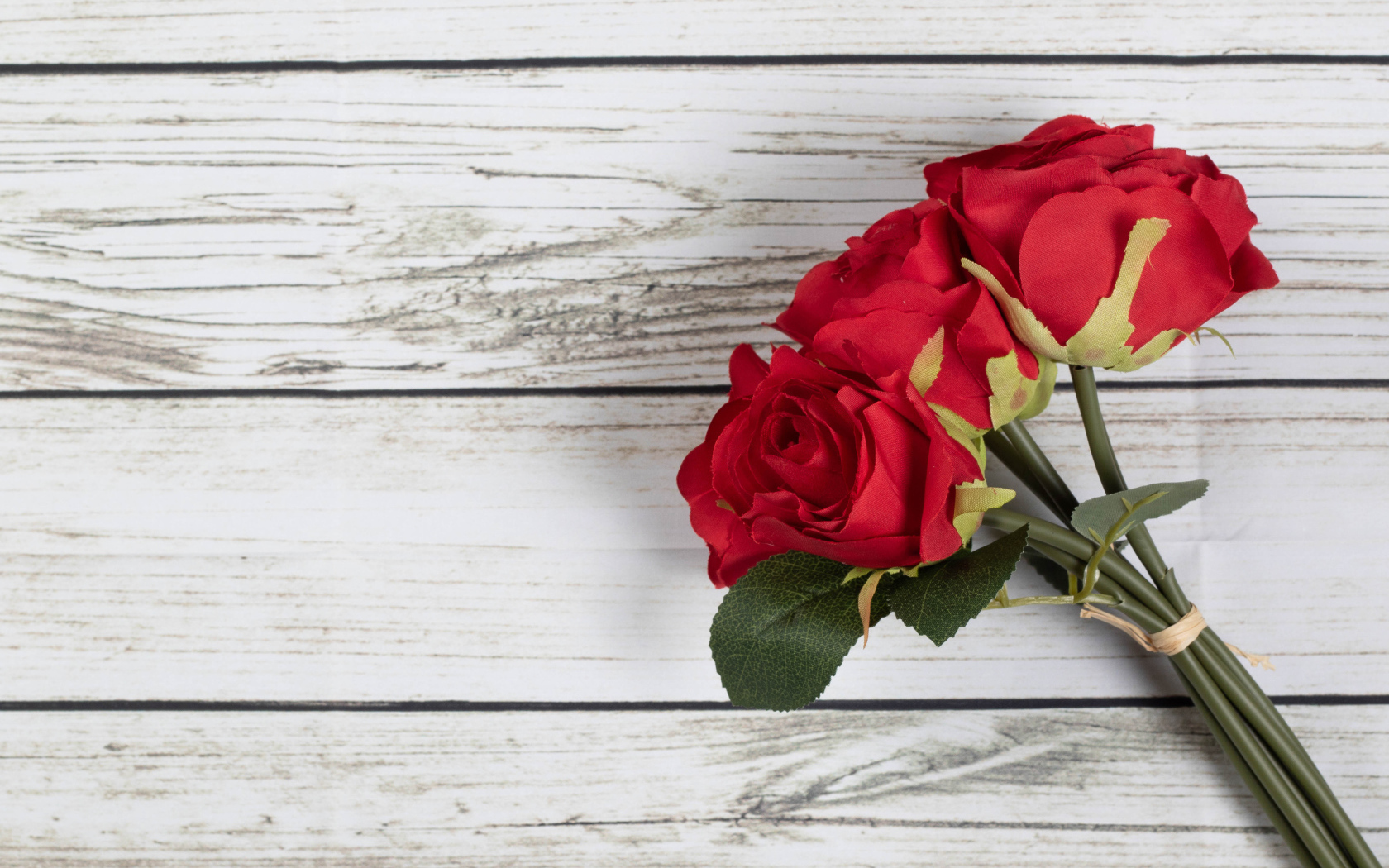 Три искусственные красные розы на деревянном фоне