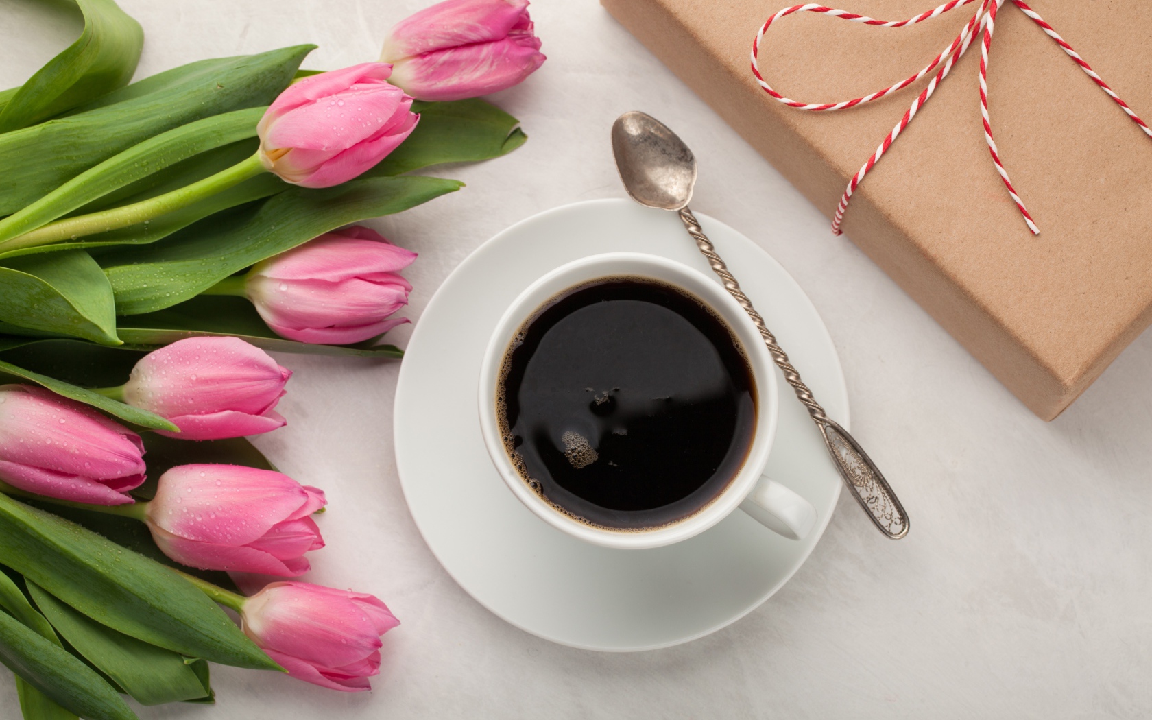 Белая чашка кофе на столе букетом розовых тюльпанов и подарком