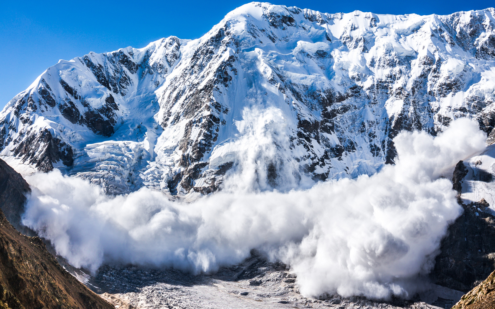 A large white avalanche descends from the snowy Alps