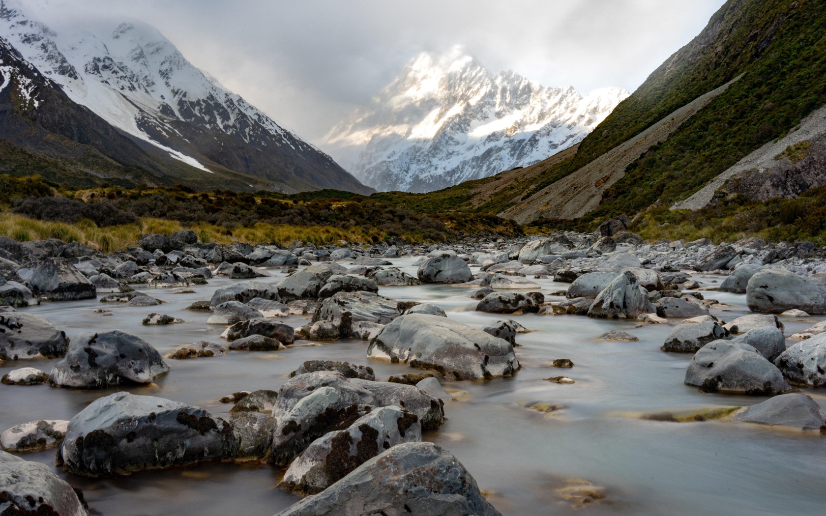 Камни в воде у заснеженных гор 