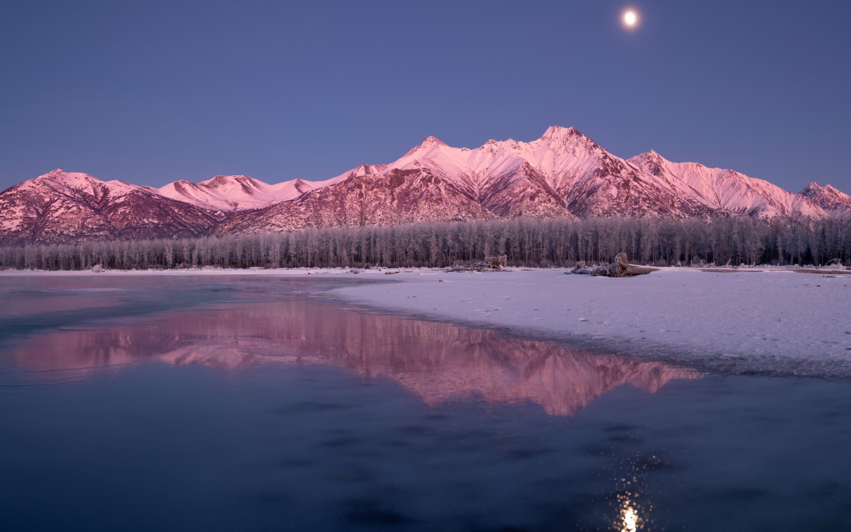 Луна над заснеженными горами отражается в заледеневшем озере 