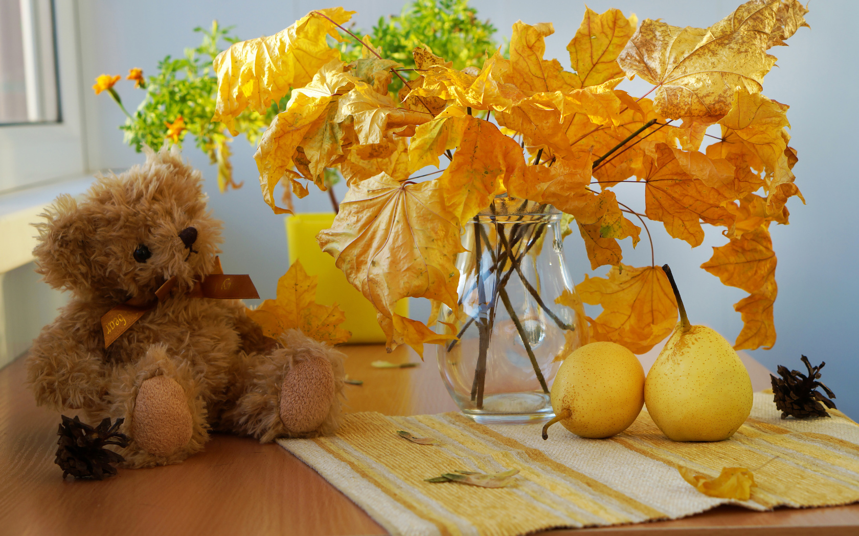 Игрушечный медведь на столе с желтыми осенними листьями и грушами