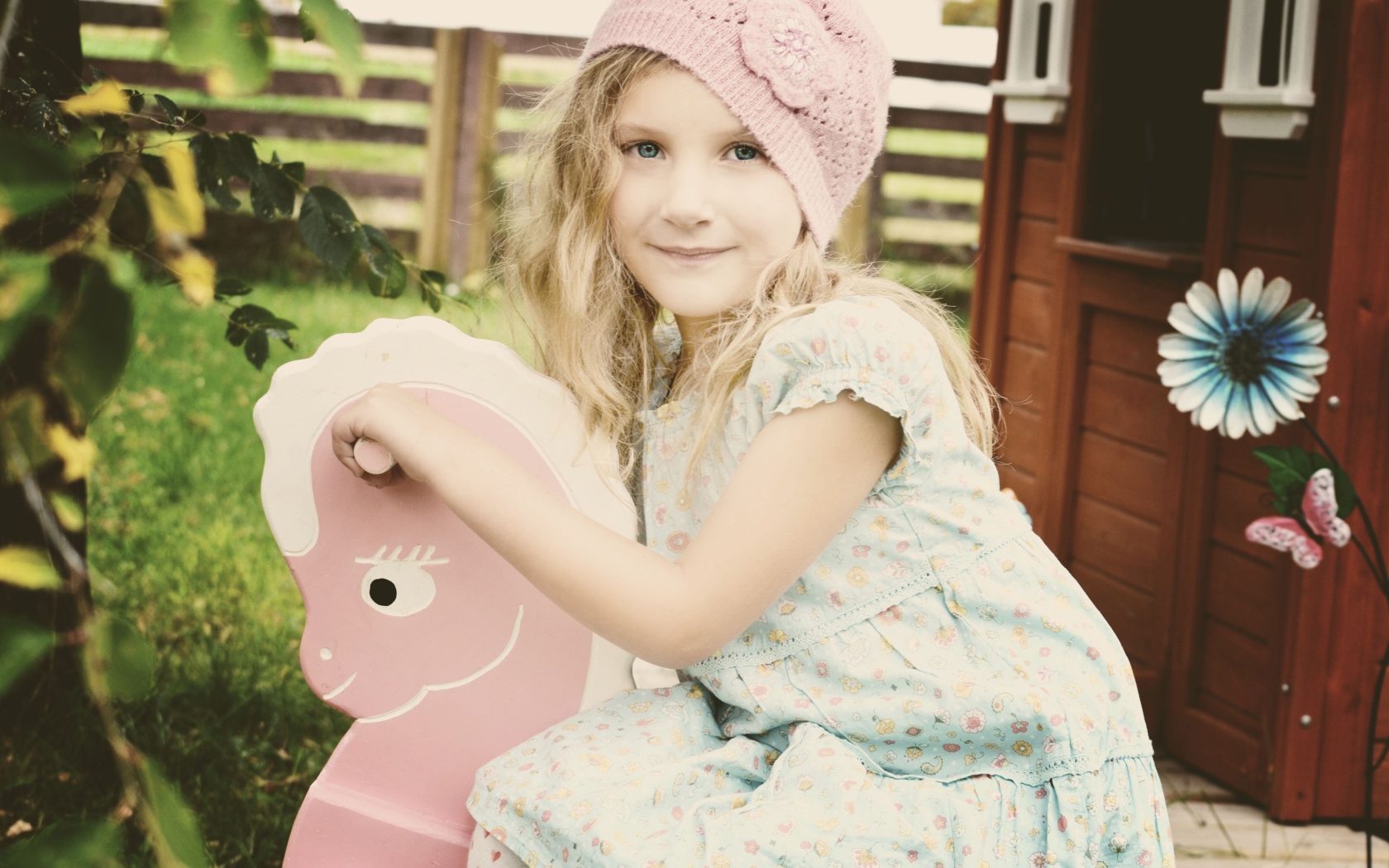 Девочка в платье сидит на деревянной лошади