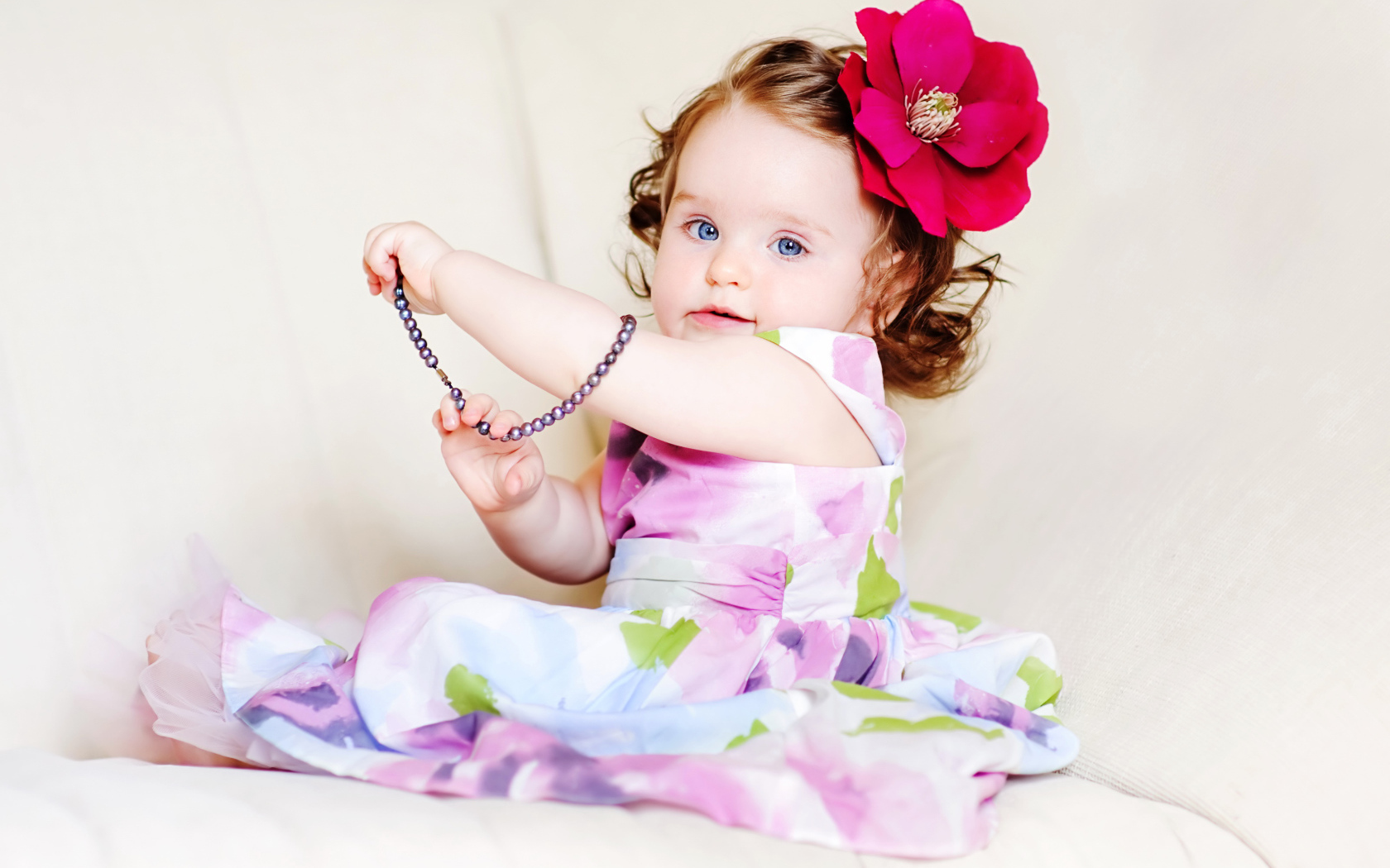 Милая голубоглазая малышка с большим красным цветком в волосах