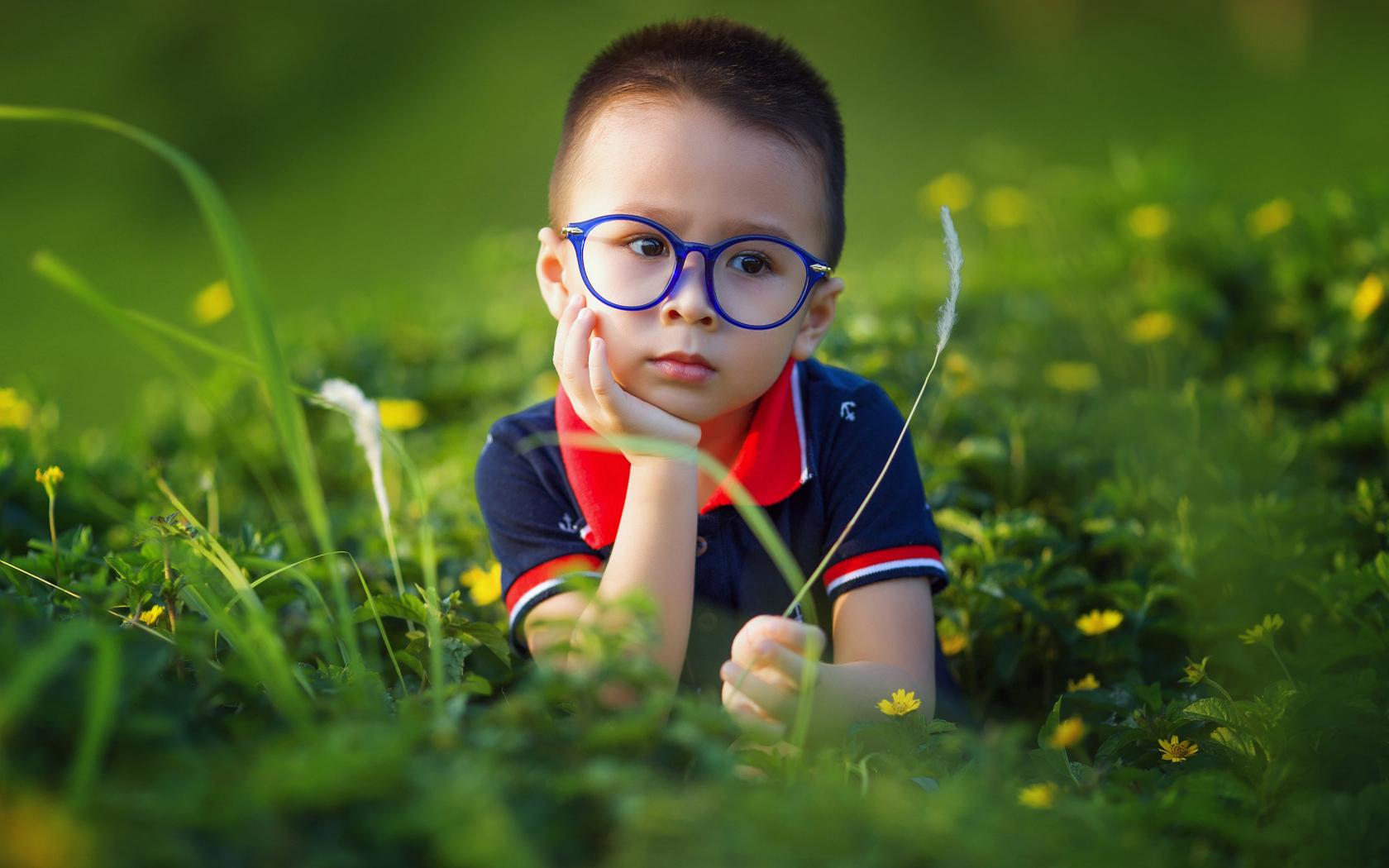 Маленький мальчик в очках лежит на зеленой траве