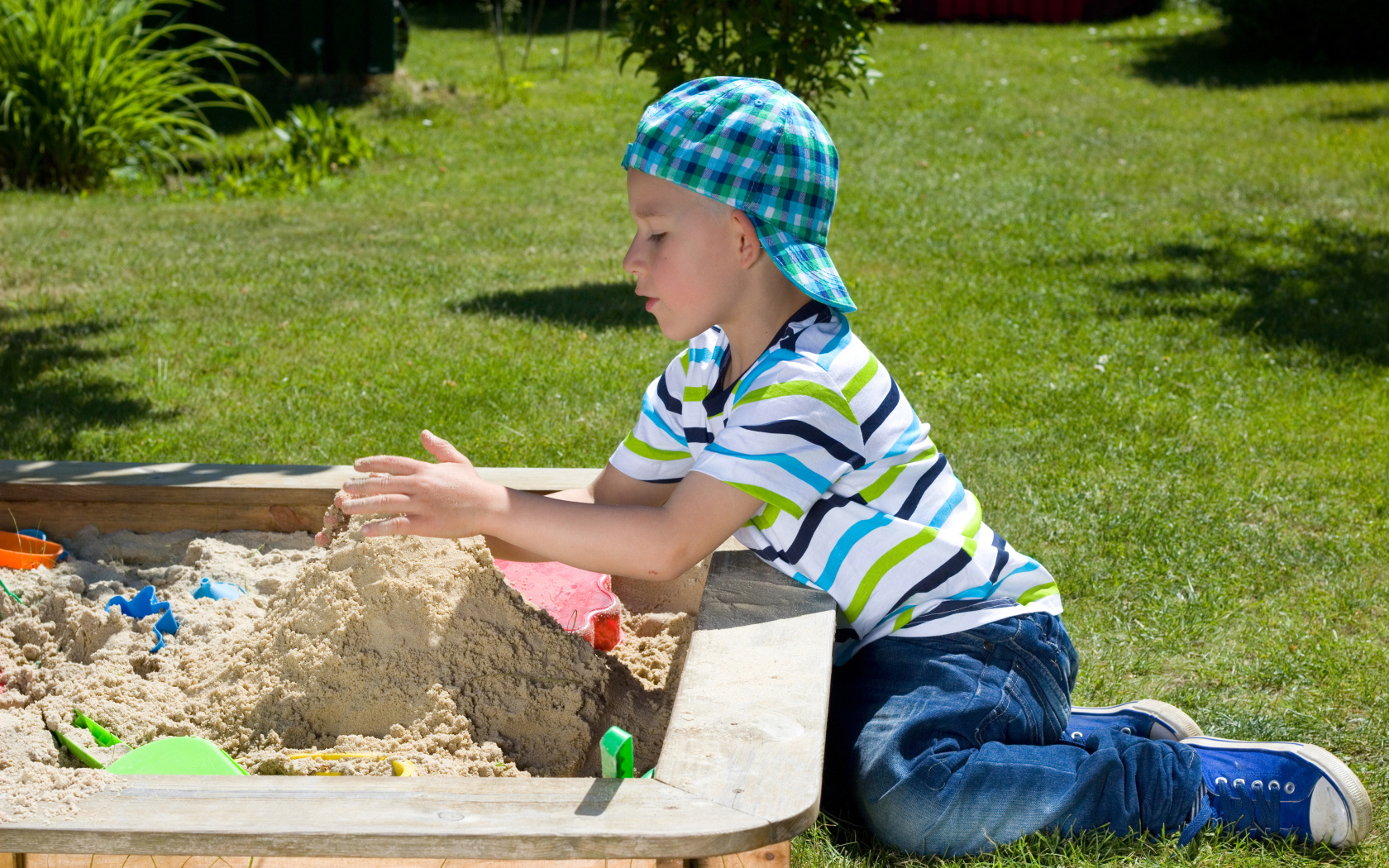 Маленький мальчик играет в песке на зеленой траве