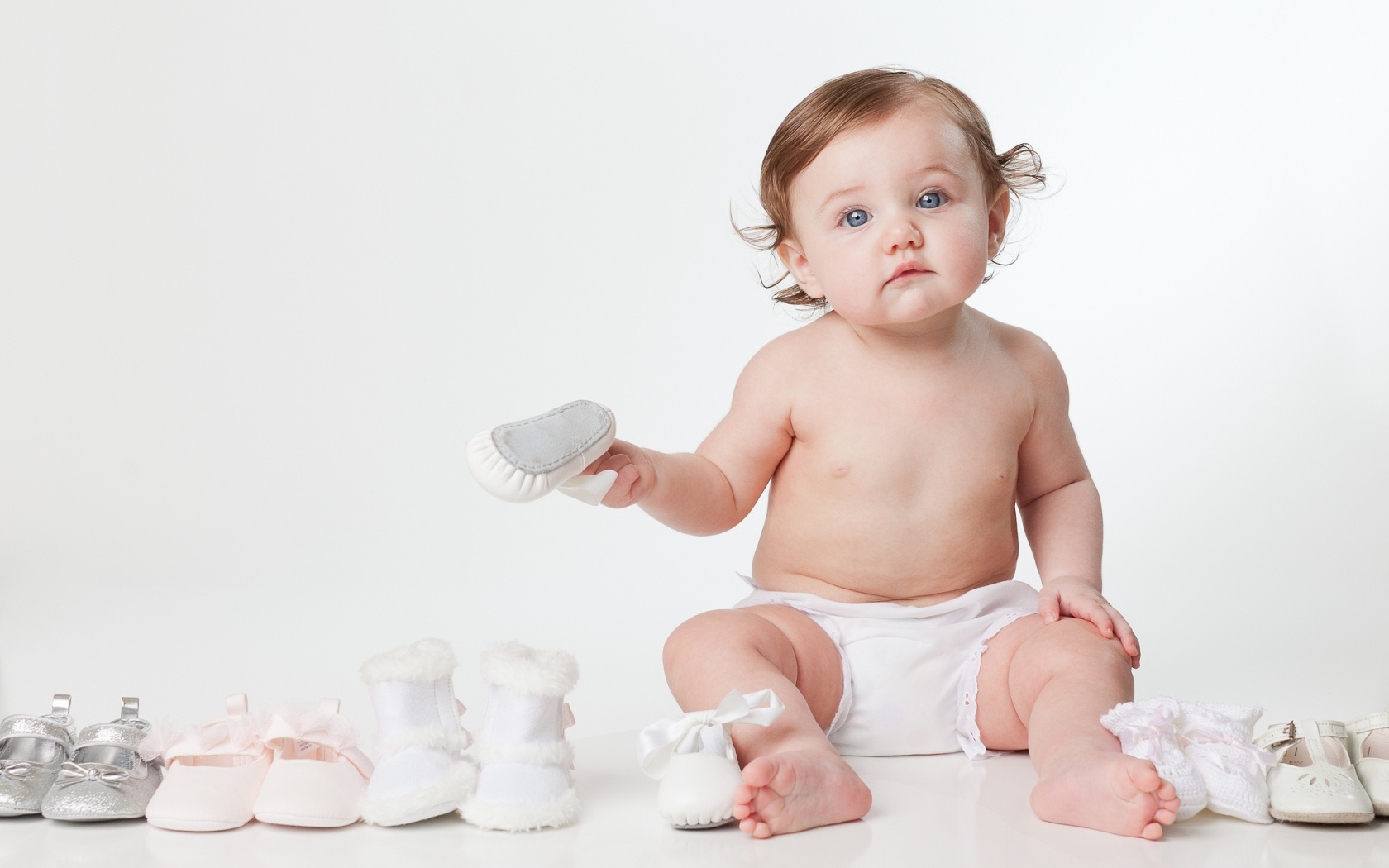 Маленький забавный голубоглазый малыш с обувью на белом фоне