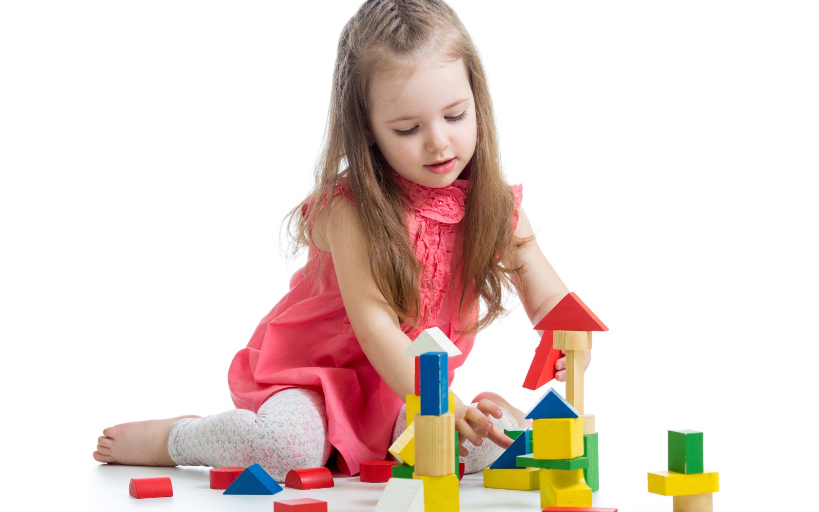 Маленькая девочка строит домик из кубиков на белом фоне