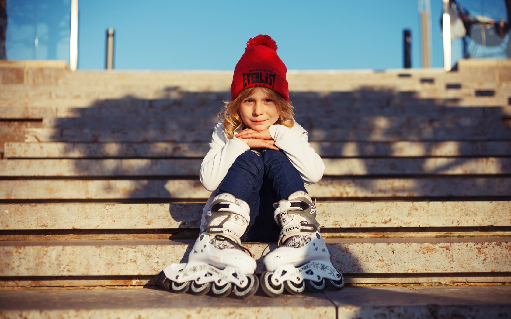 Маленькая девочка в роликах сидит на ступеньках 