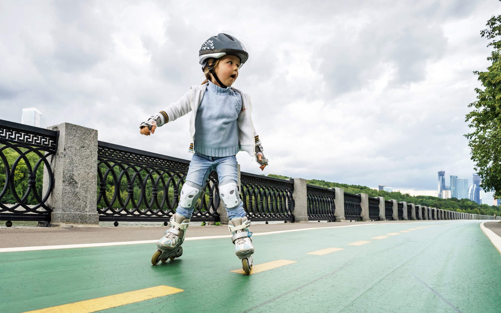 Маленькая девочка катается по мосту на роликах