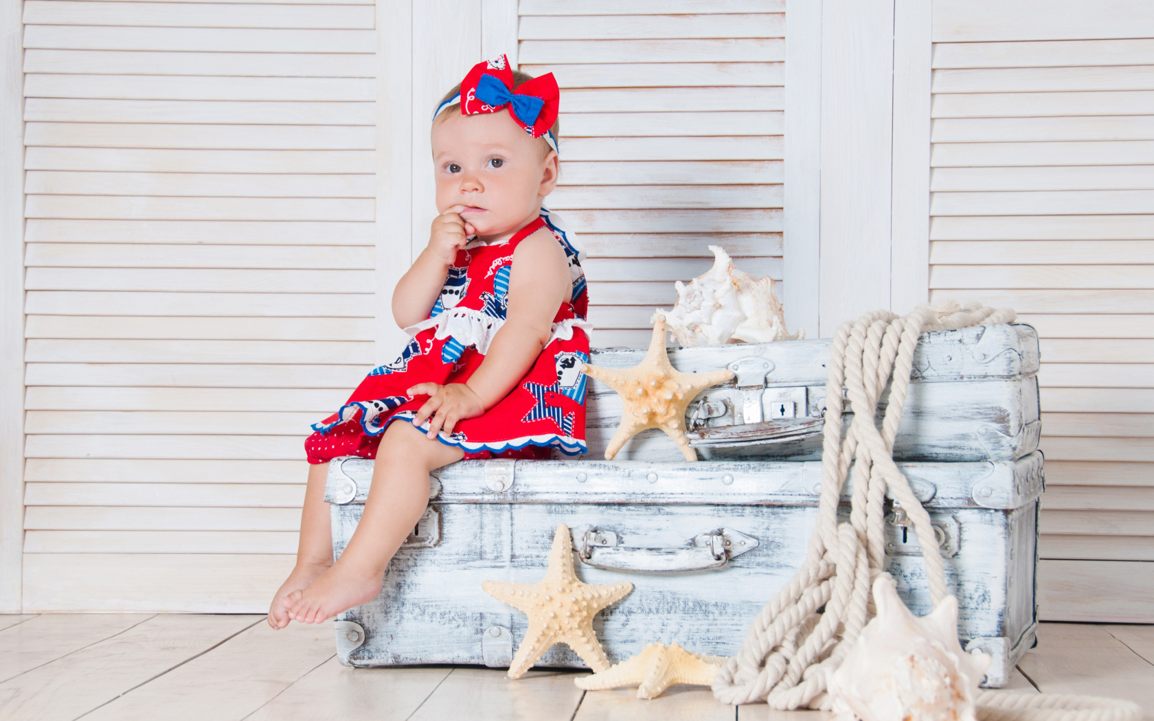 Маленькая девочка сидит на чемодане с морскими звездами