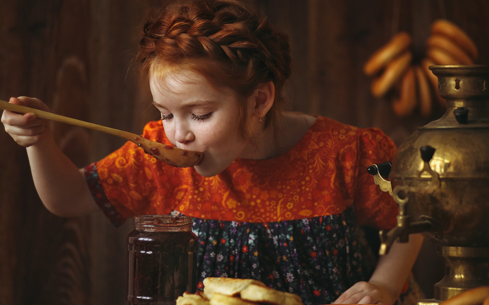 Маленькая рыжеволосая девочка пробует варенье