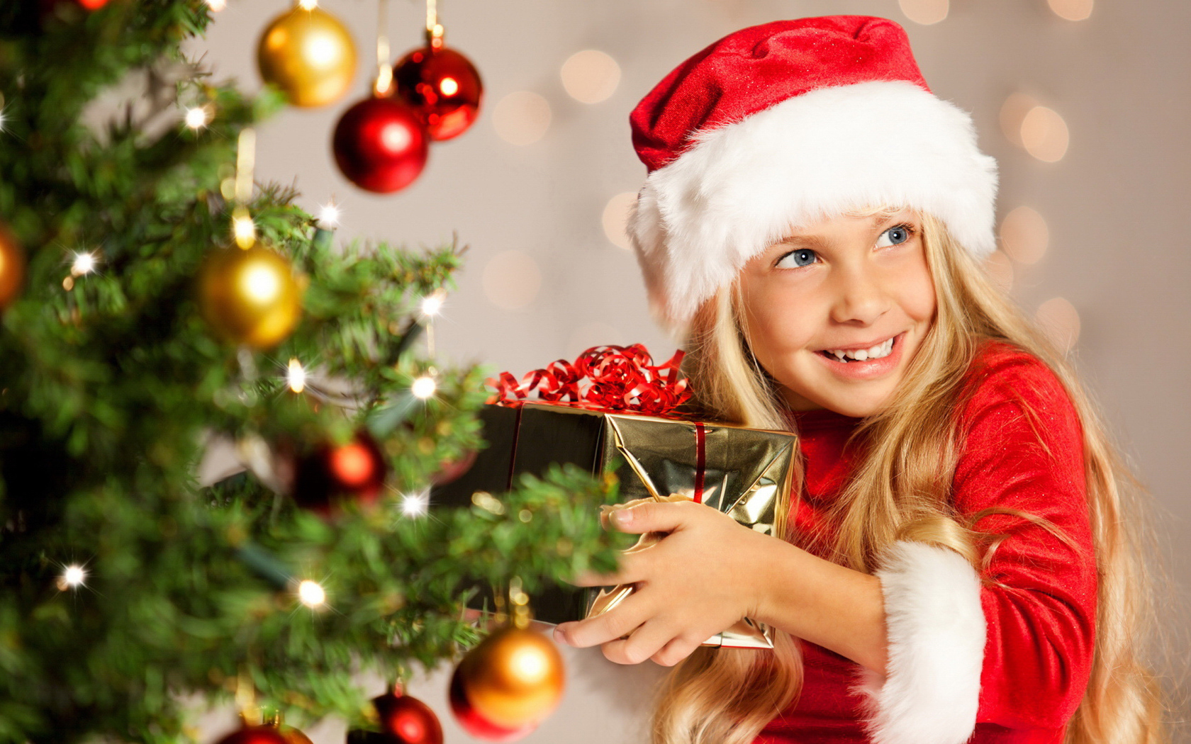 Улыбающаяся девочка блондинка с подарком у елки на новый год 