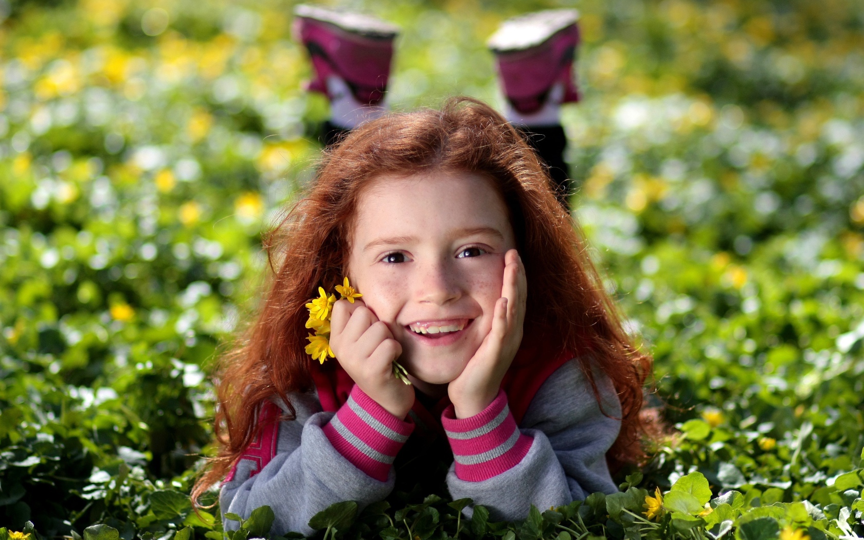 Улыбающаяся рыжеволосая девочка лежит на зеленой траве