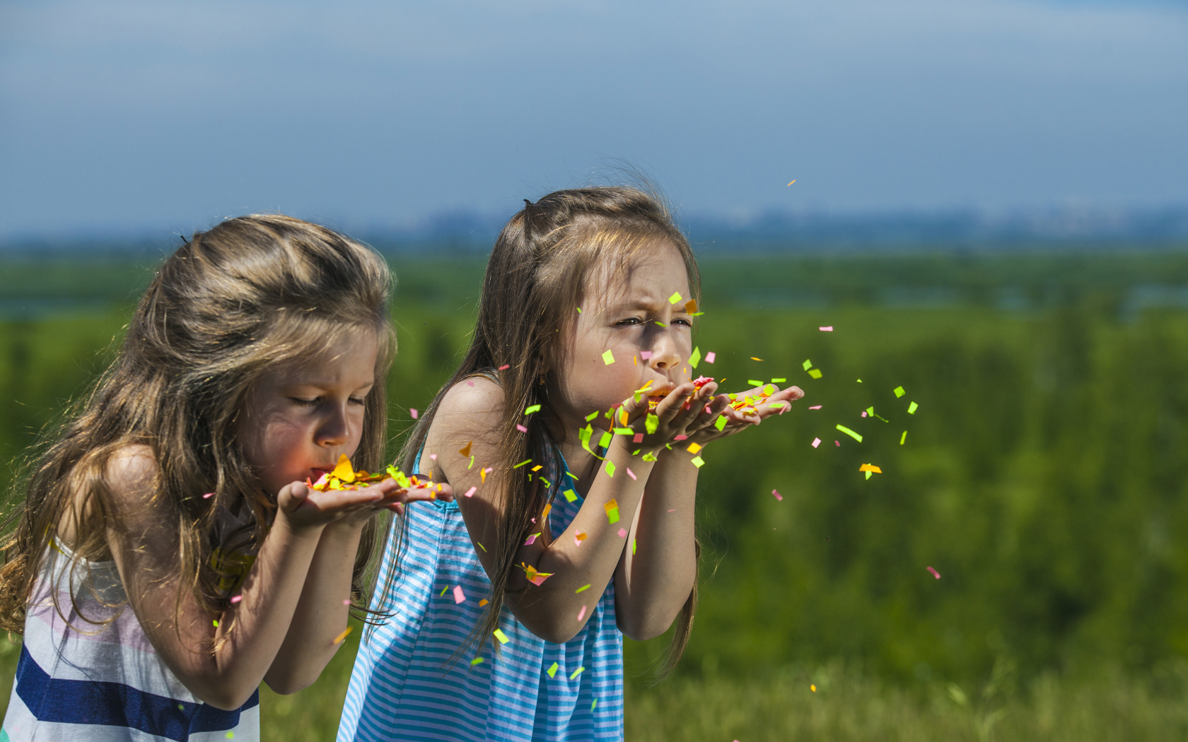 Две маленькие девочки сдувают конфетти  с рук