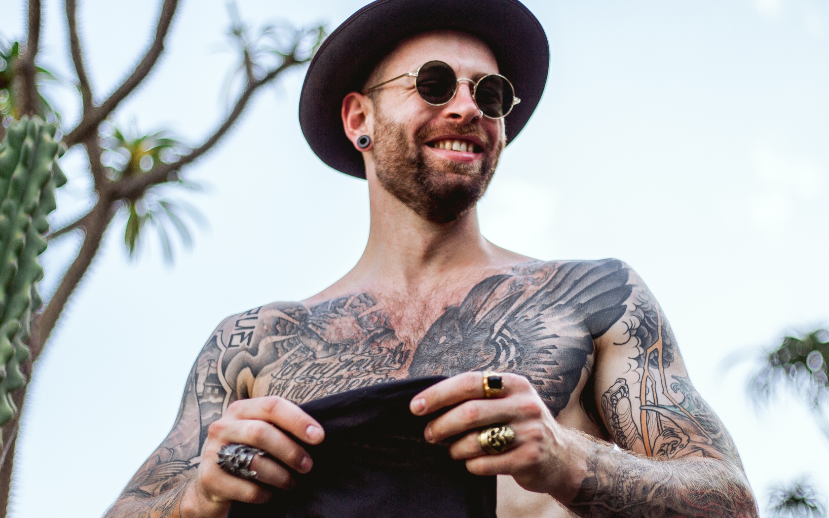 Мужчина с татуировками на теле в черной шляпе и очках