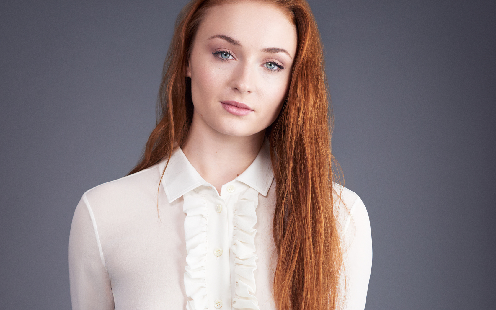 Рыжеволосая голубоглазая актриса Софи Тёрнер на сером фоне