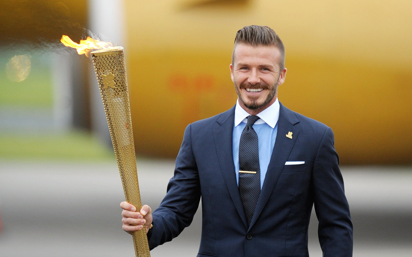 Улыбающийся футболист Дэвид Бекхэм с олимпийский огнем в руке