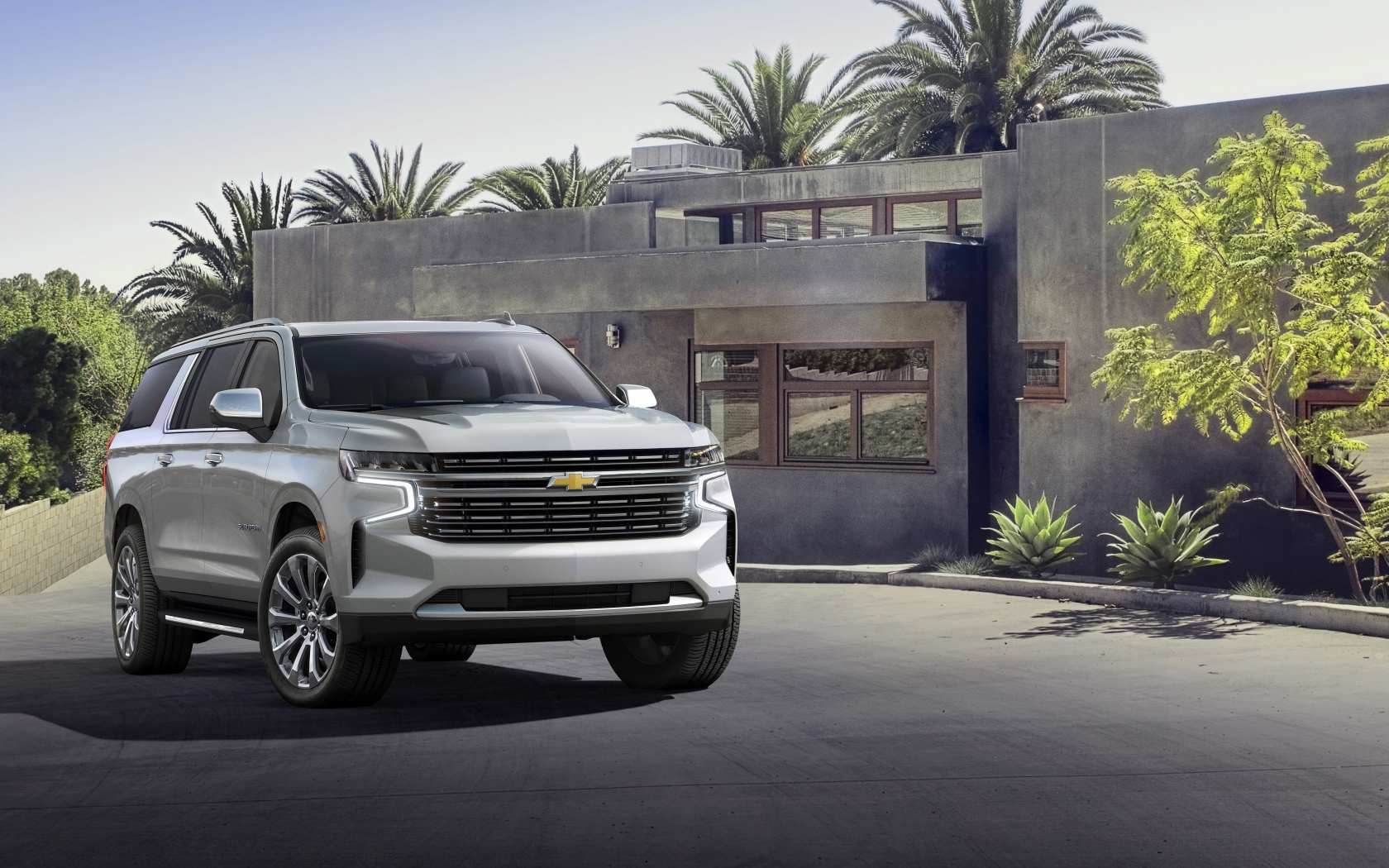 Серый внедорожник Chevrolet Suburban, 2021 года на фоне дома