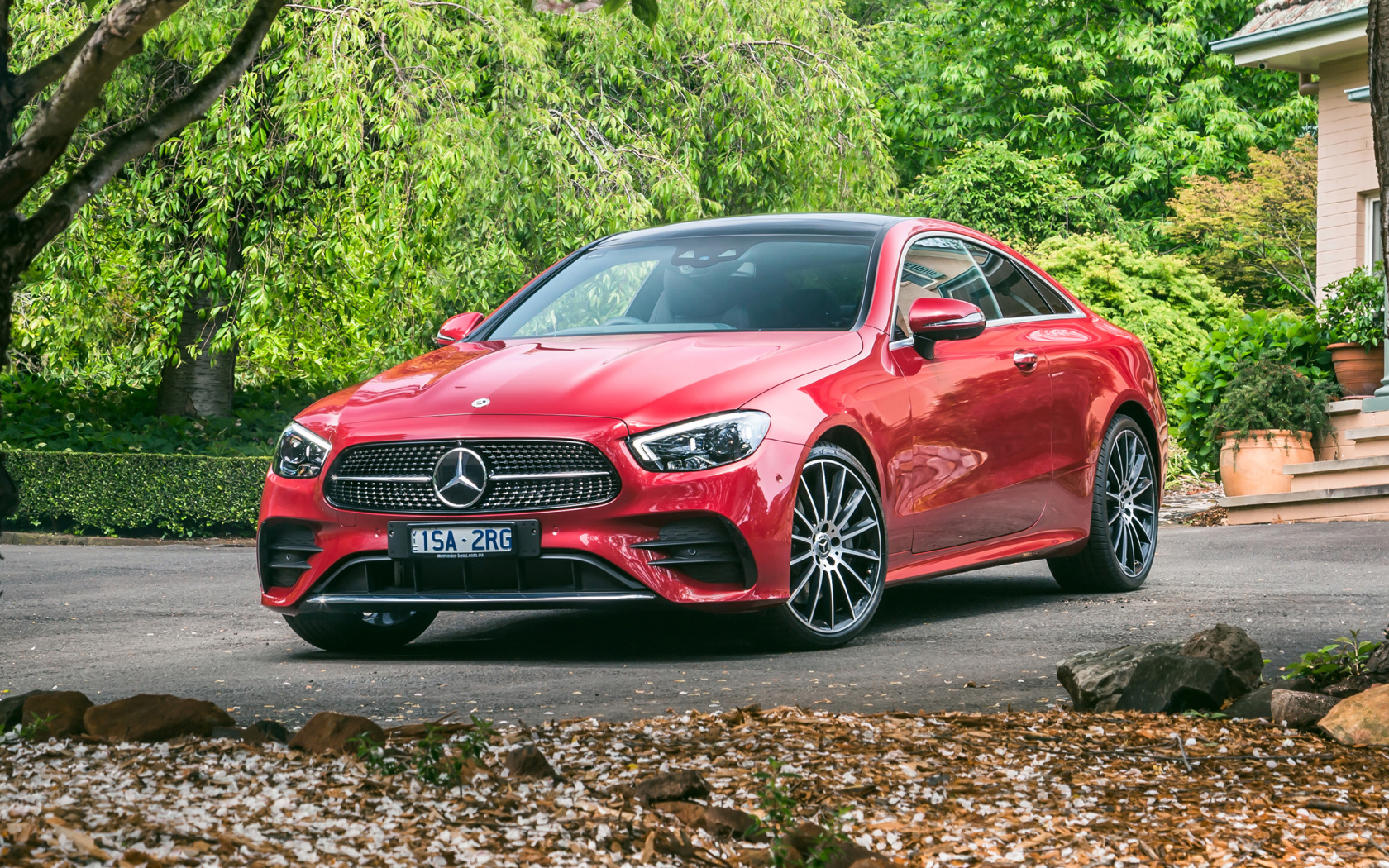 Красный автомобиль Mercedes-Benz E 300 AMG, 2020 года у дома осенью