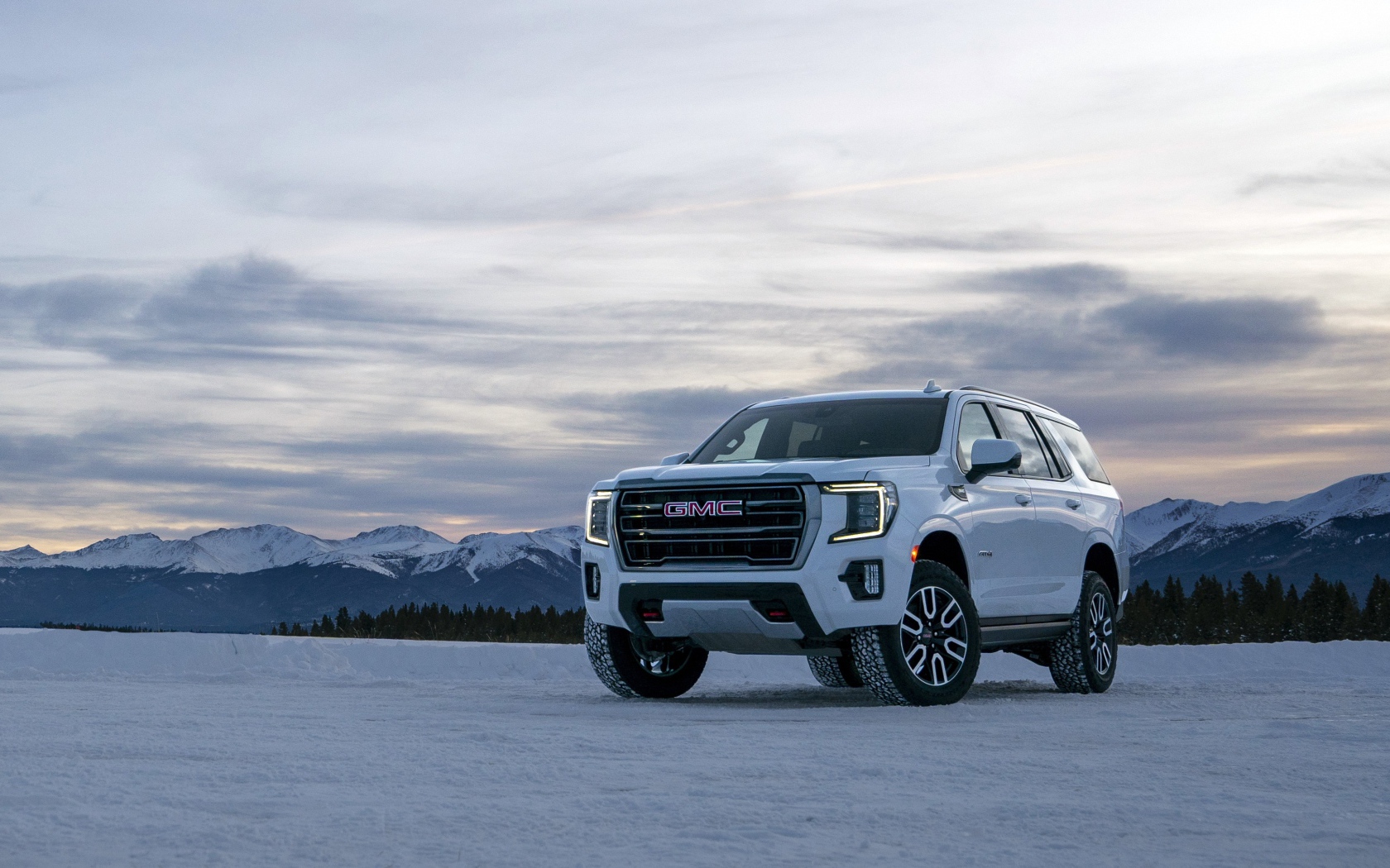 Белый внедорожник  GMC Yukon AT4, 2021 года на фоне заснеженных гор 