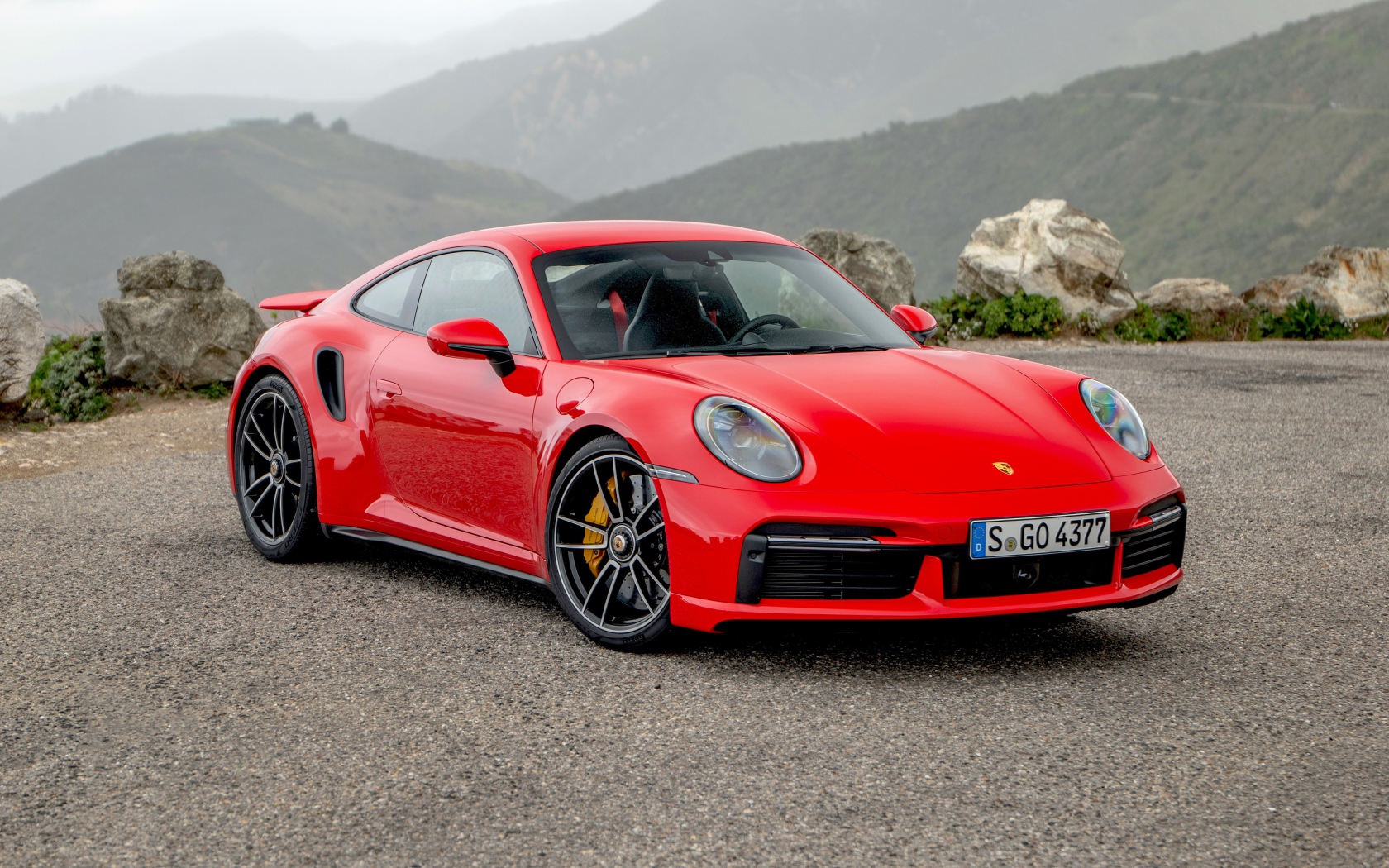 Красный автомобиль Porsche 911 Turbo S 2020 года на фоне гор 