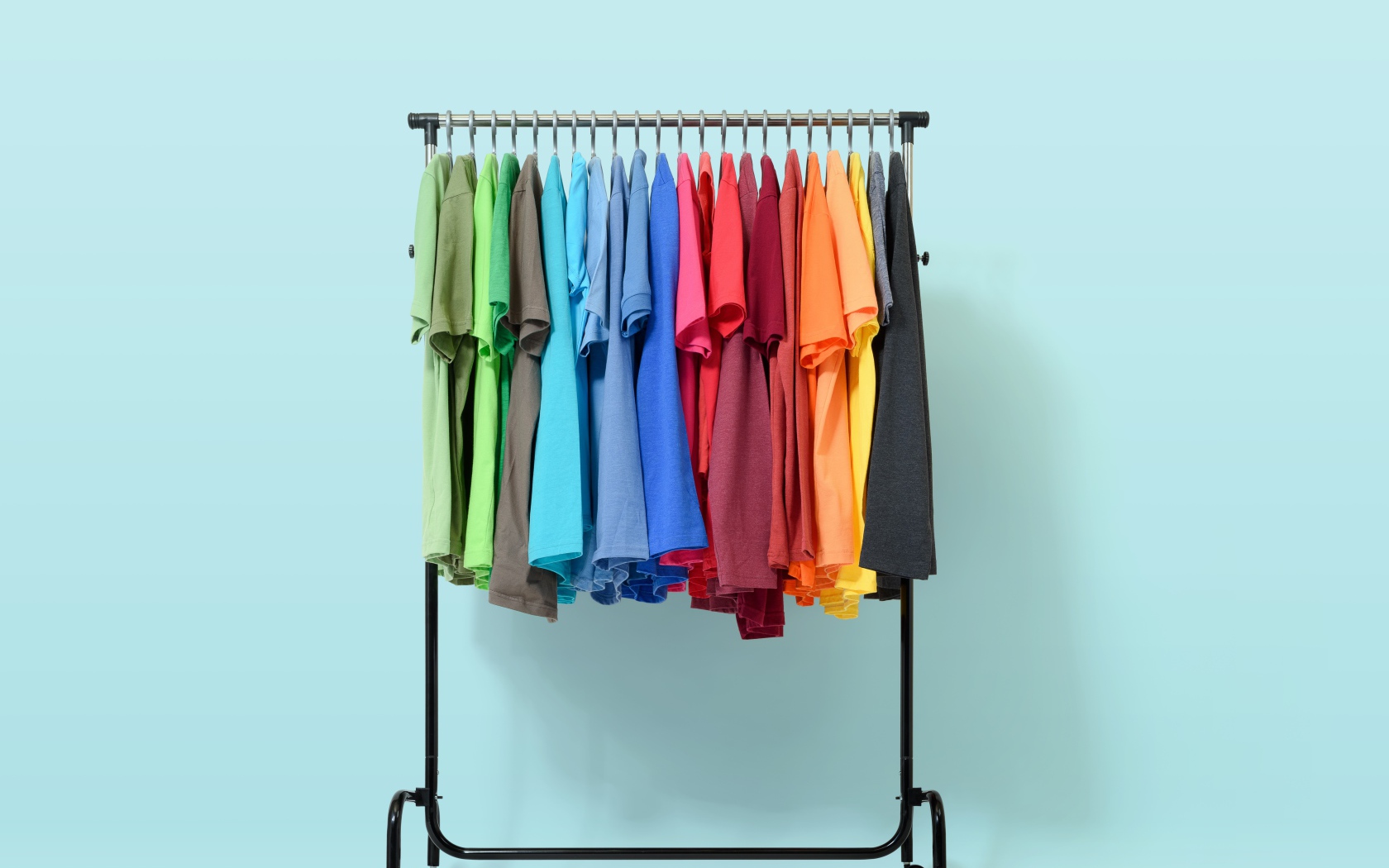 Разноцветные футболки на вешалке на голубом фоне