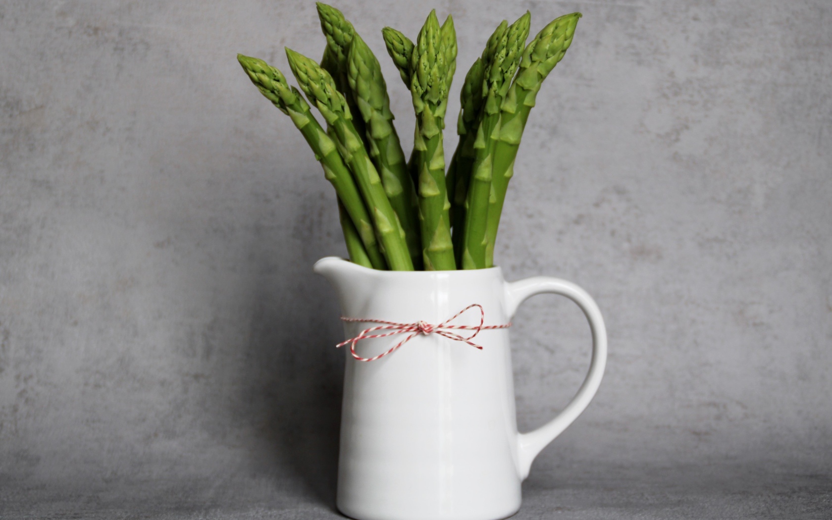 Зеленая спаржа в белой вазе на фоне серой стены