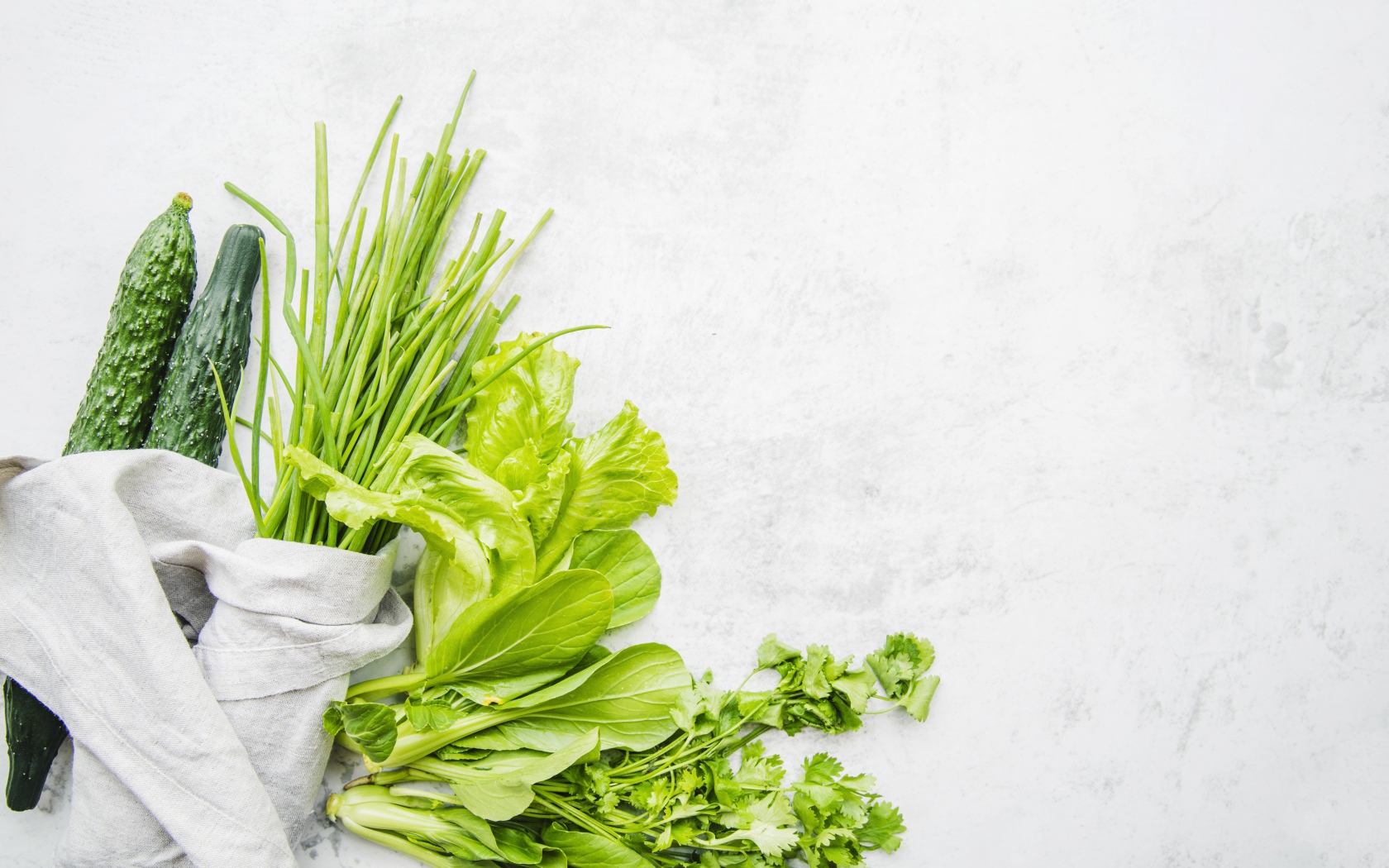 Зелень петрушки и лука, листья салата и свежие огурцы на белом фоне