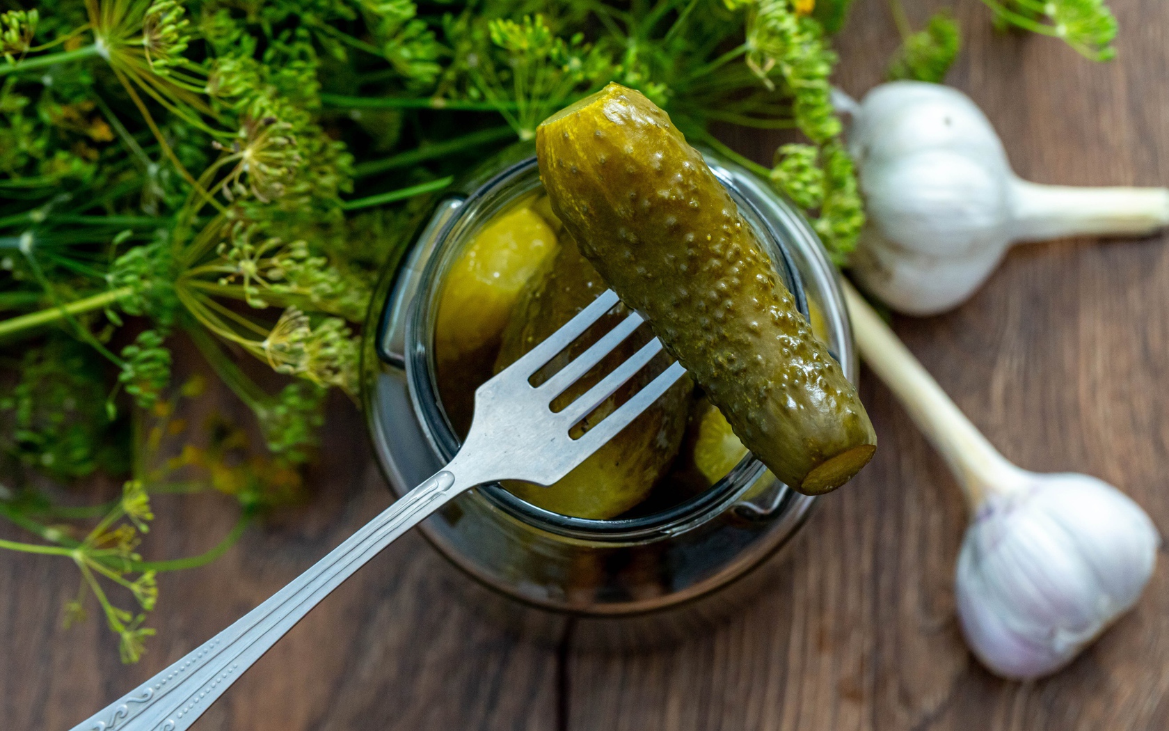 Маринованные огурцы в банке на столе с чесноком и укропом