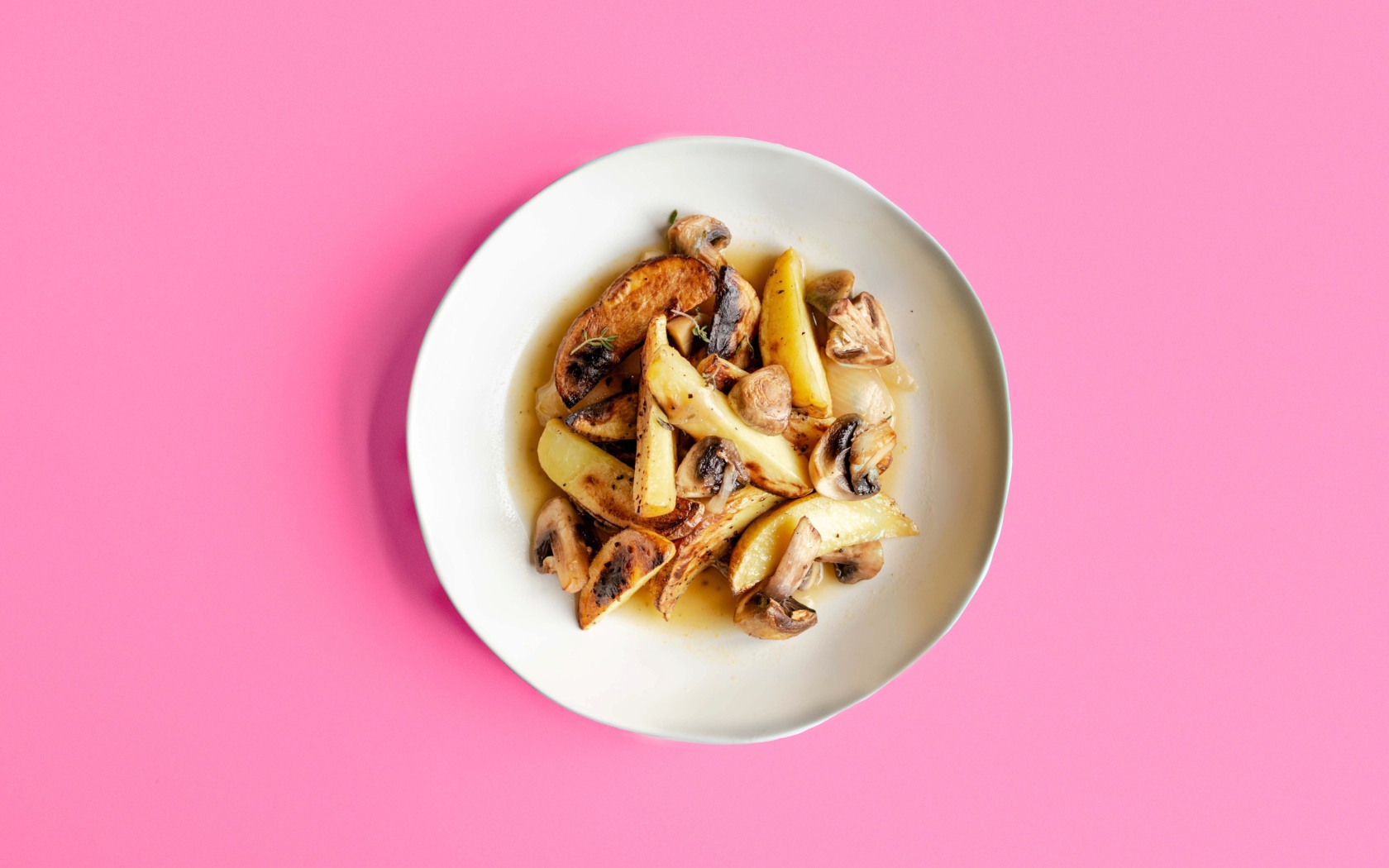 Картофель с грибами в тарелке на розовом фоне 