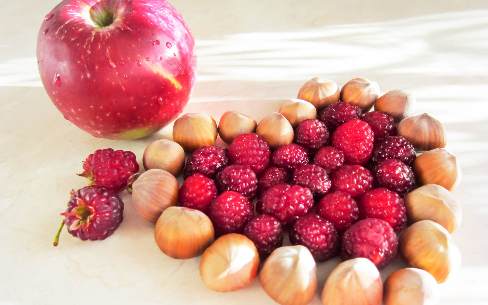 Сердце из лесных орехов и малины на столе с красным яблоком