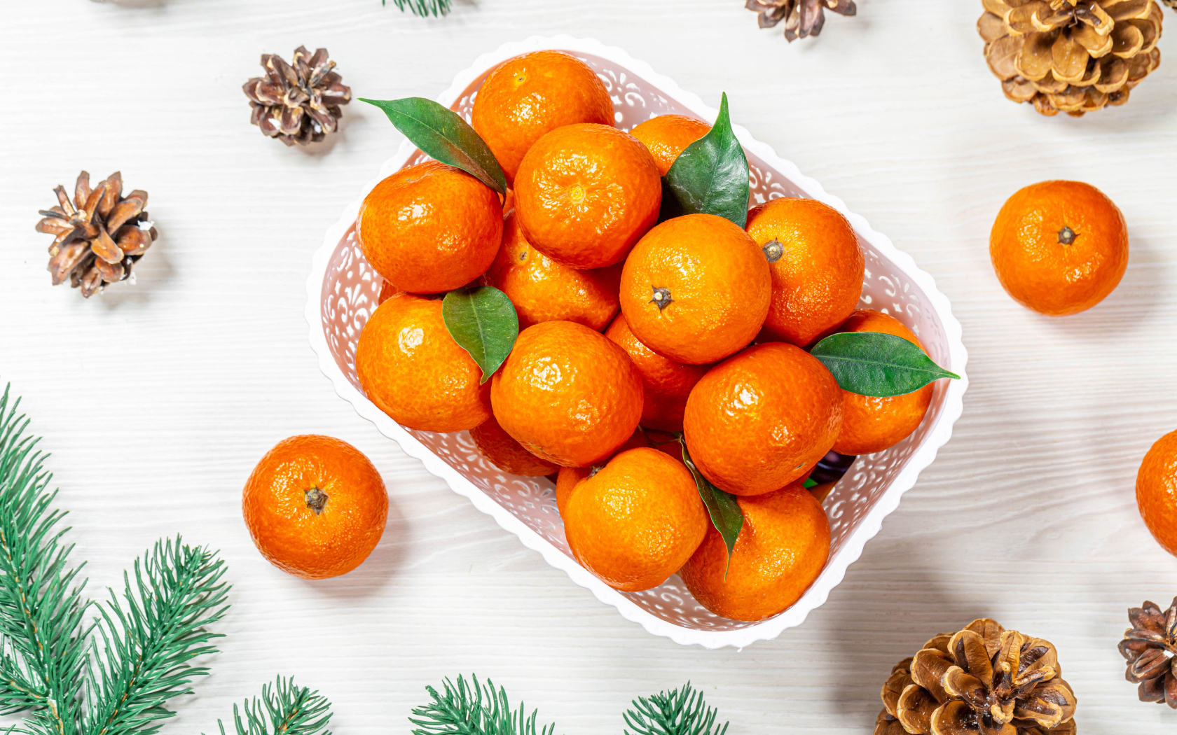 Много спелых мандаринов в белой корзинке на столе с шишками